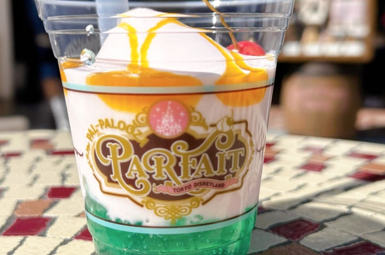 プラスチックカップに入ったパフェがテーブルに置かれている。上にソースとチェリーがトッピングされている。