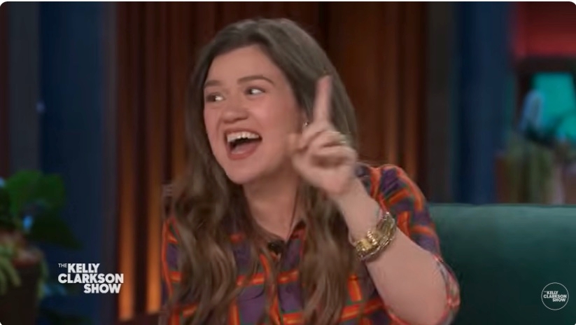 Kelly Clarkson gesturing and smiling on "The Kelly Clarkson Show." Wearing a plaid shirt and multiple bracelets
