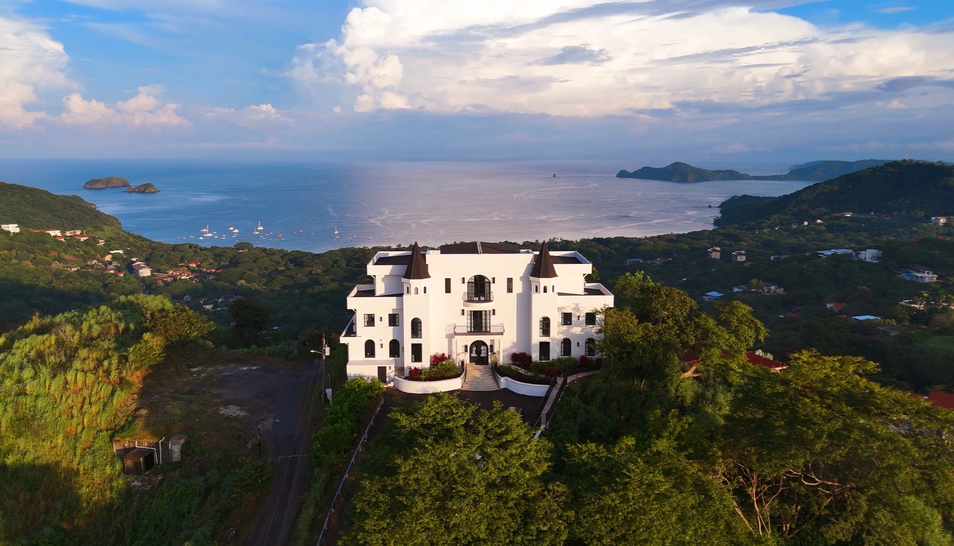 Large achromatic  mansion overlooks water  and lush greenish  landscape, with distant   islands and a partially  cloudy entity  successful  the background