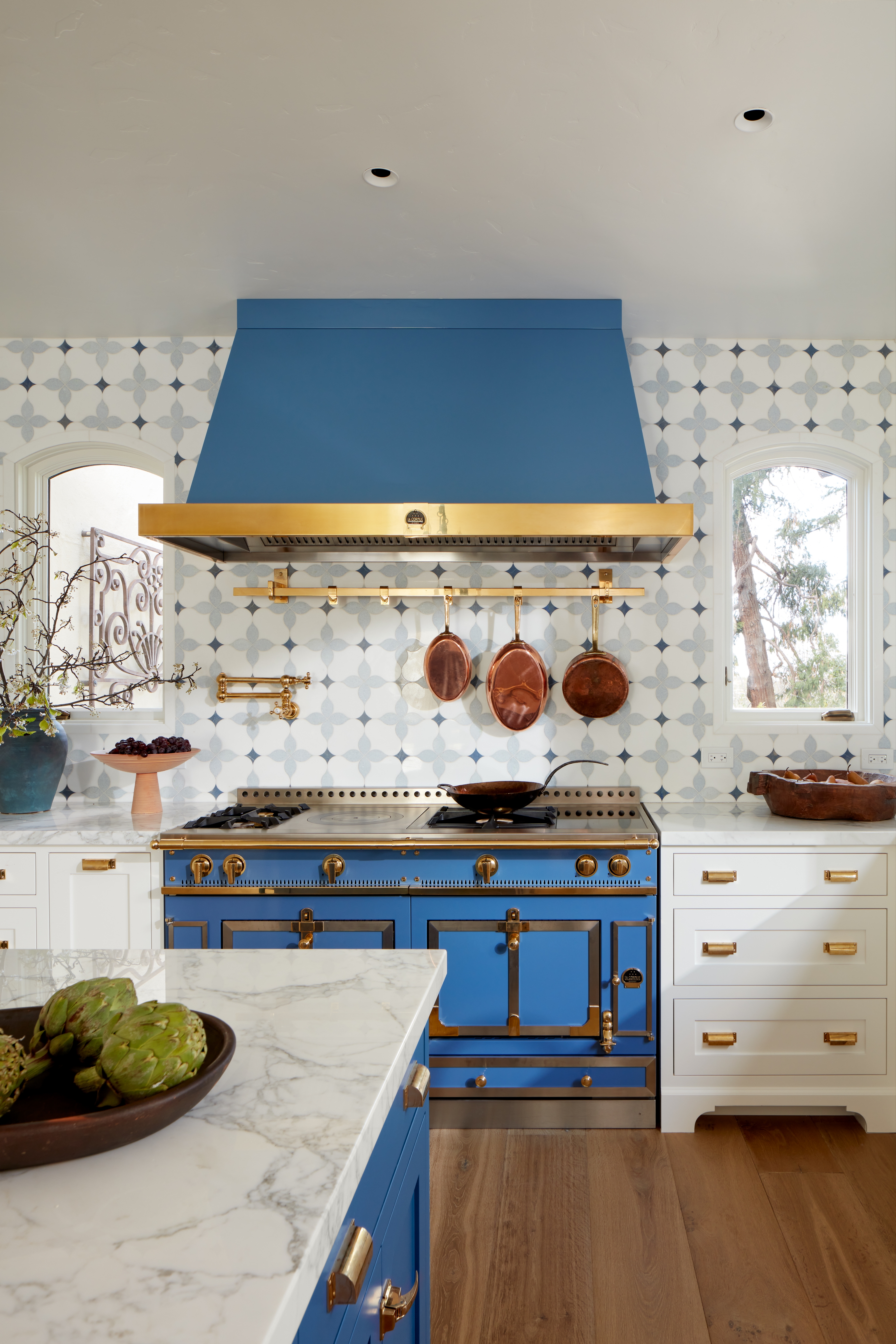 Stylish room  with a bluish  and brass stove, patterned backsplash, marble countertops, and decorative items connected  counters