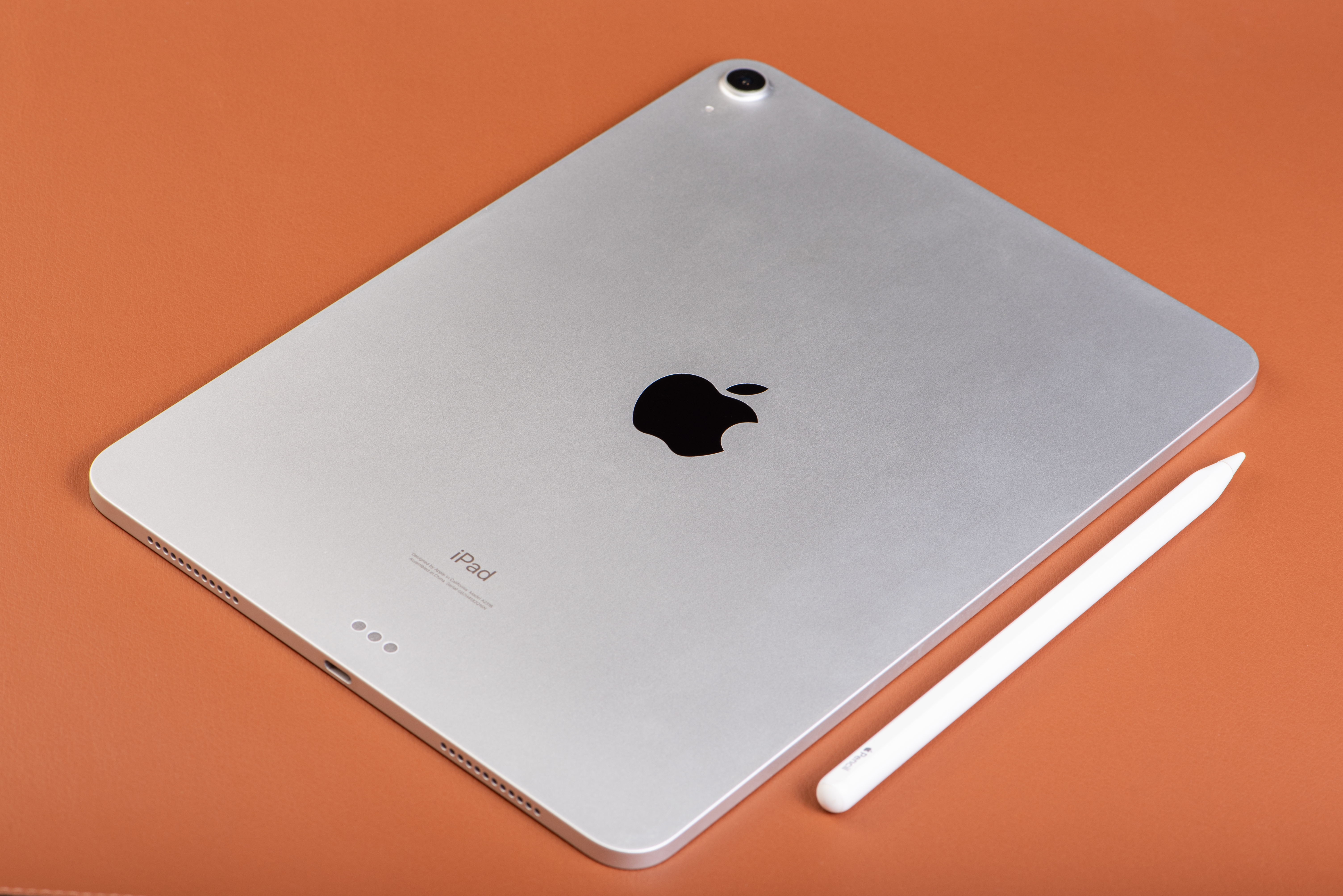 A metallic  iPad placed connected  a level  aboveground  adjacent  to a achromatic  stylus, viewed from the back