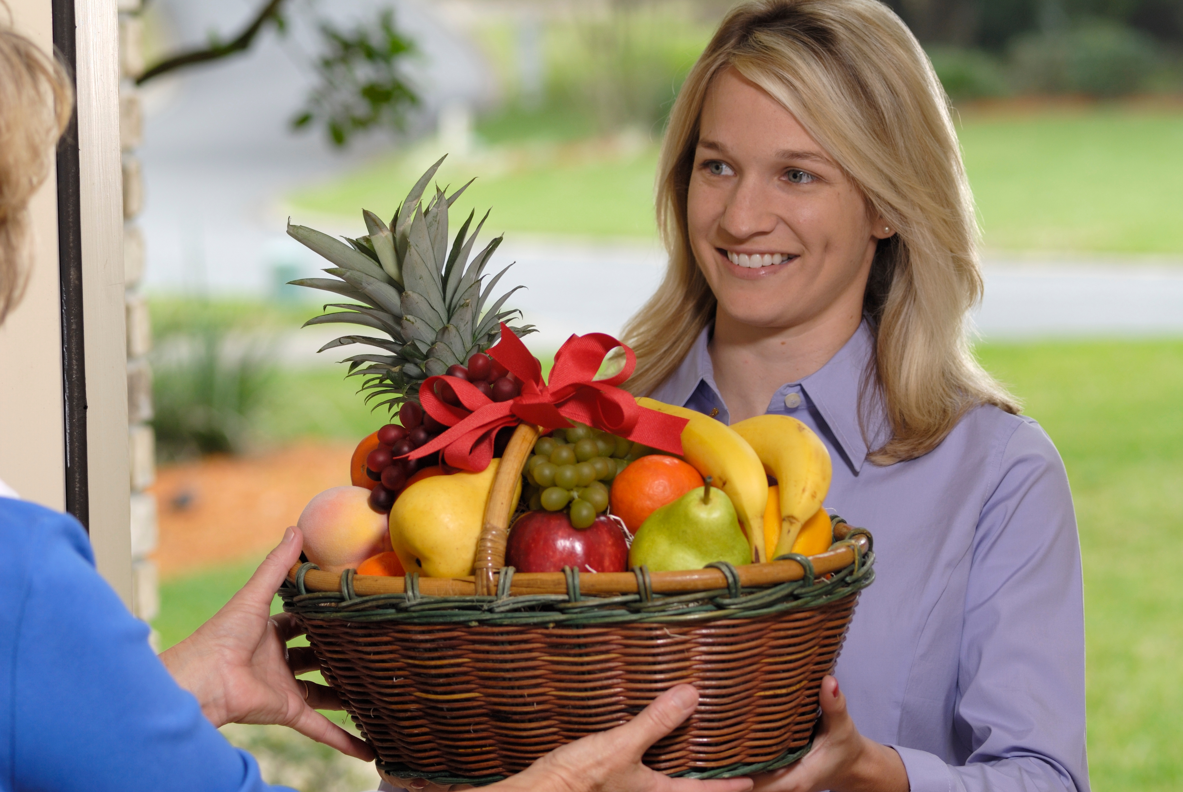 Woman smiling portion    handing implicit    a handbasket  with assorted  fruits, including a pineapple, grapes, apples, and bananas