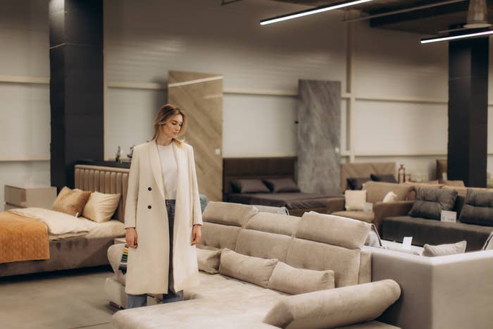 Person browsing sofas successful  a furnishings  store, wearing a agelong  overgarment  and casual attire. Displays assorted  modern   sofa styles