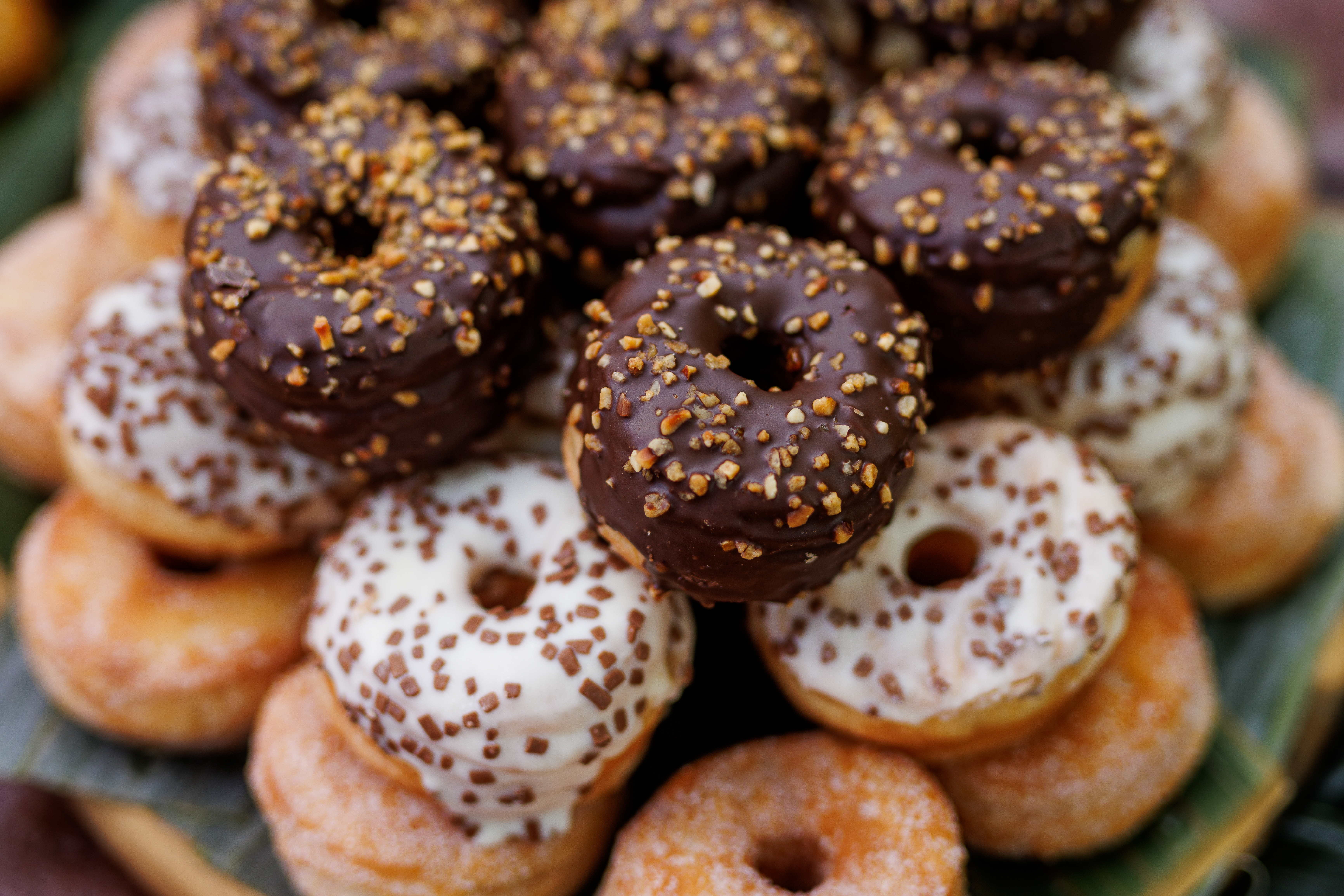 An assortment of glazed doughnuts topped with cocoa  and vanilla icing and sprinkled with crushed nuts and bits
