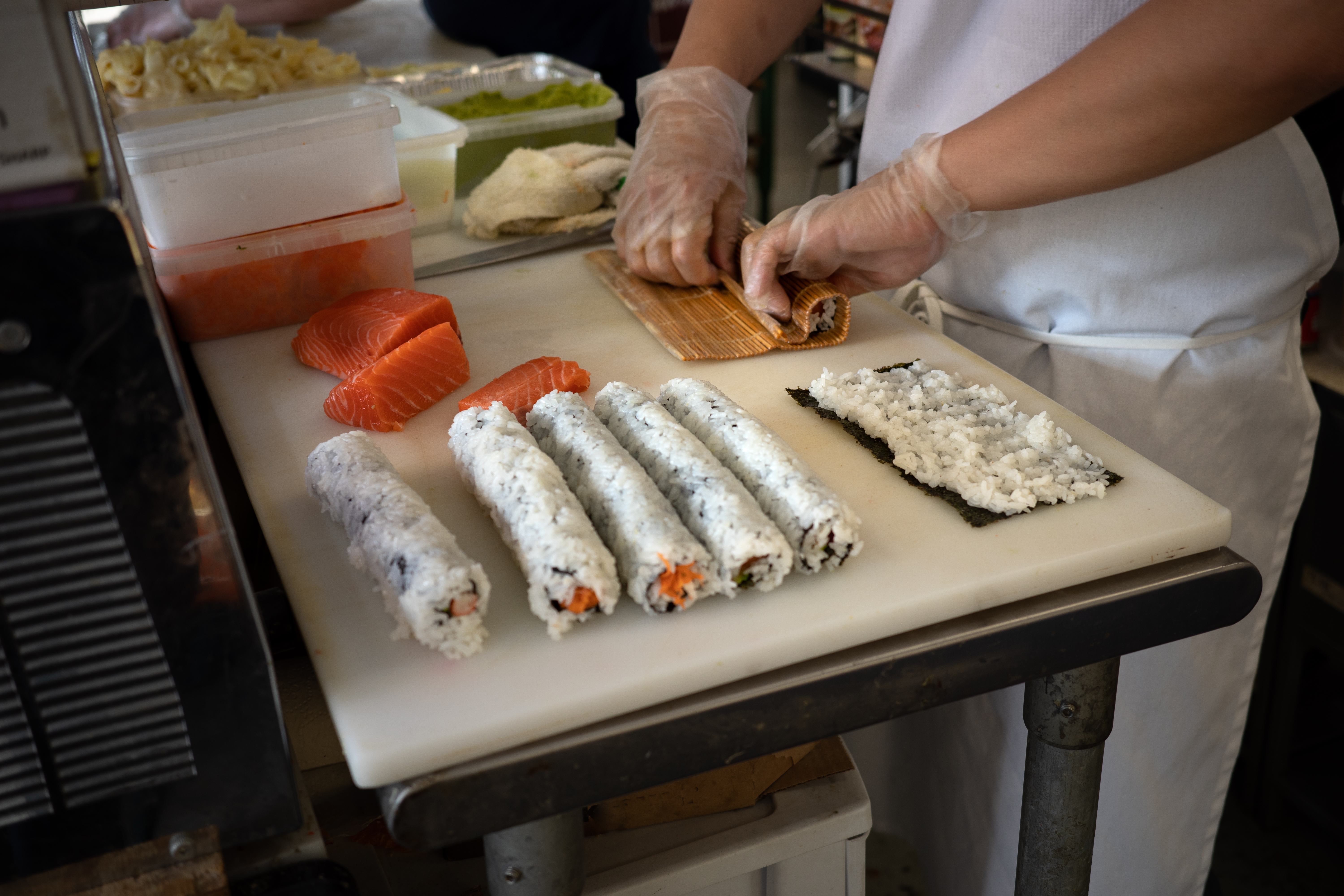 Chef rolling sushi adjacent  to prepared ingredients including salmon and rice-filled rolls connected  a room  counter