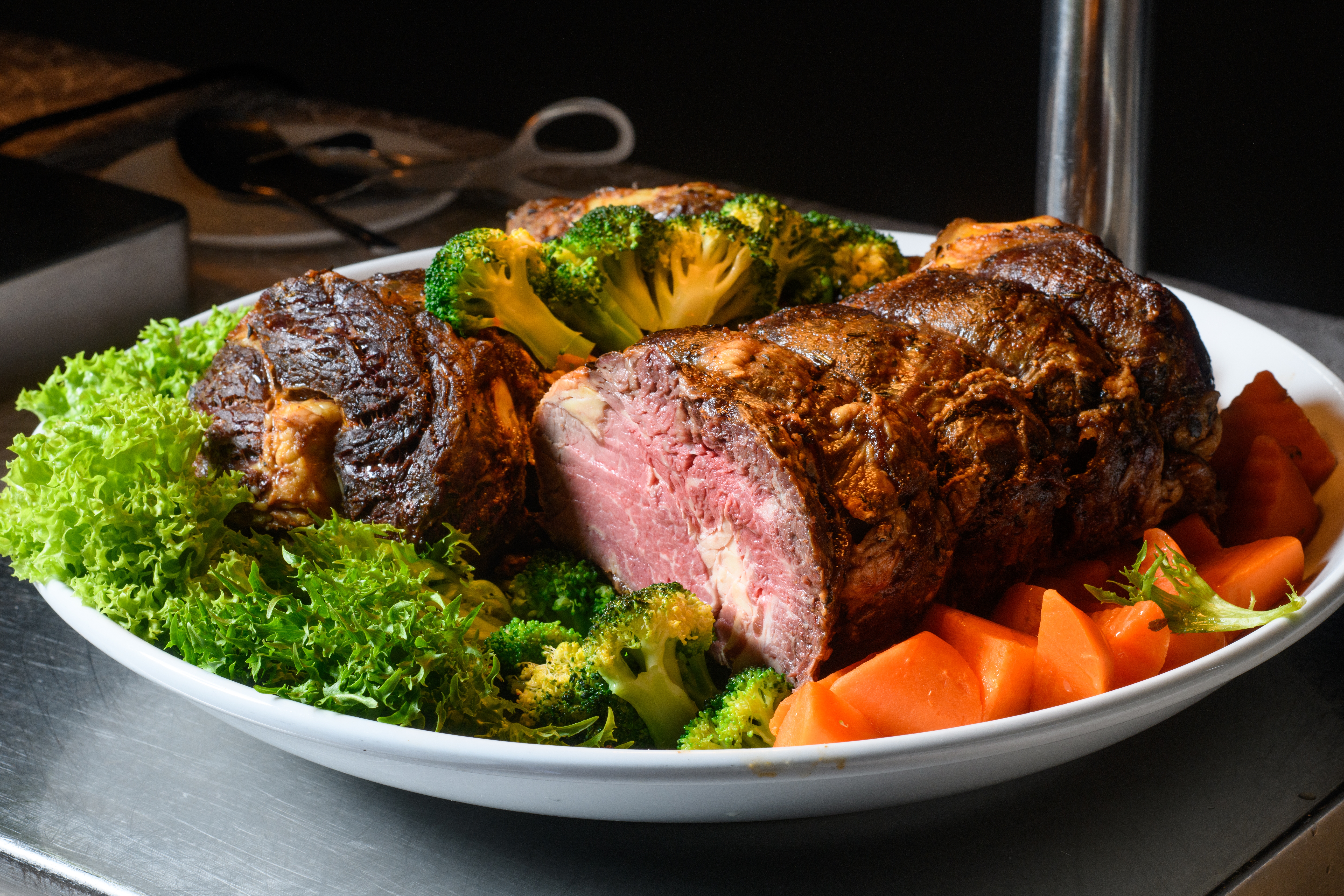 A sheet  of roast beef surrounded by broccoli, lettuce, and sliced carrots, arranged neatly for serving