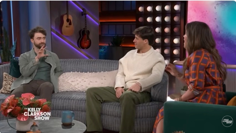 Three people, including a guest in casual attire and the host in a patterned dress, chat on the set of The Kelly Clarkson Show