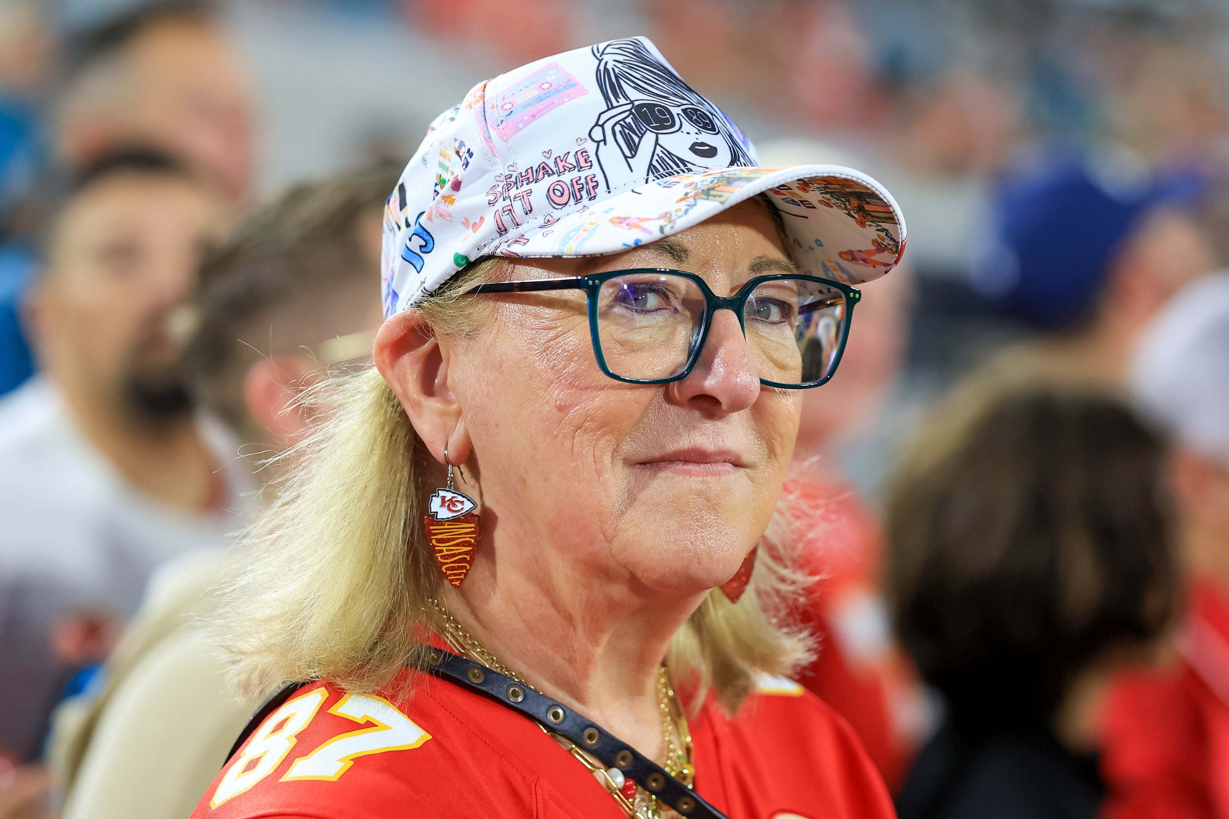 Person i dekorativ caps og sportstrøye, iført briller og øredobber, på et arrangement