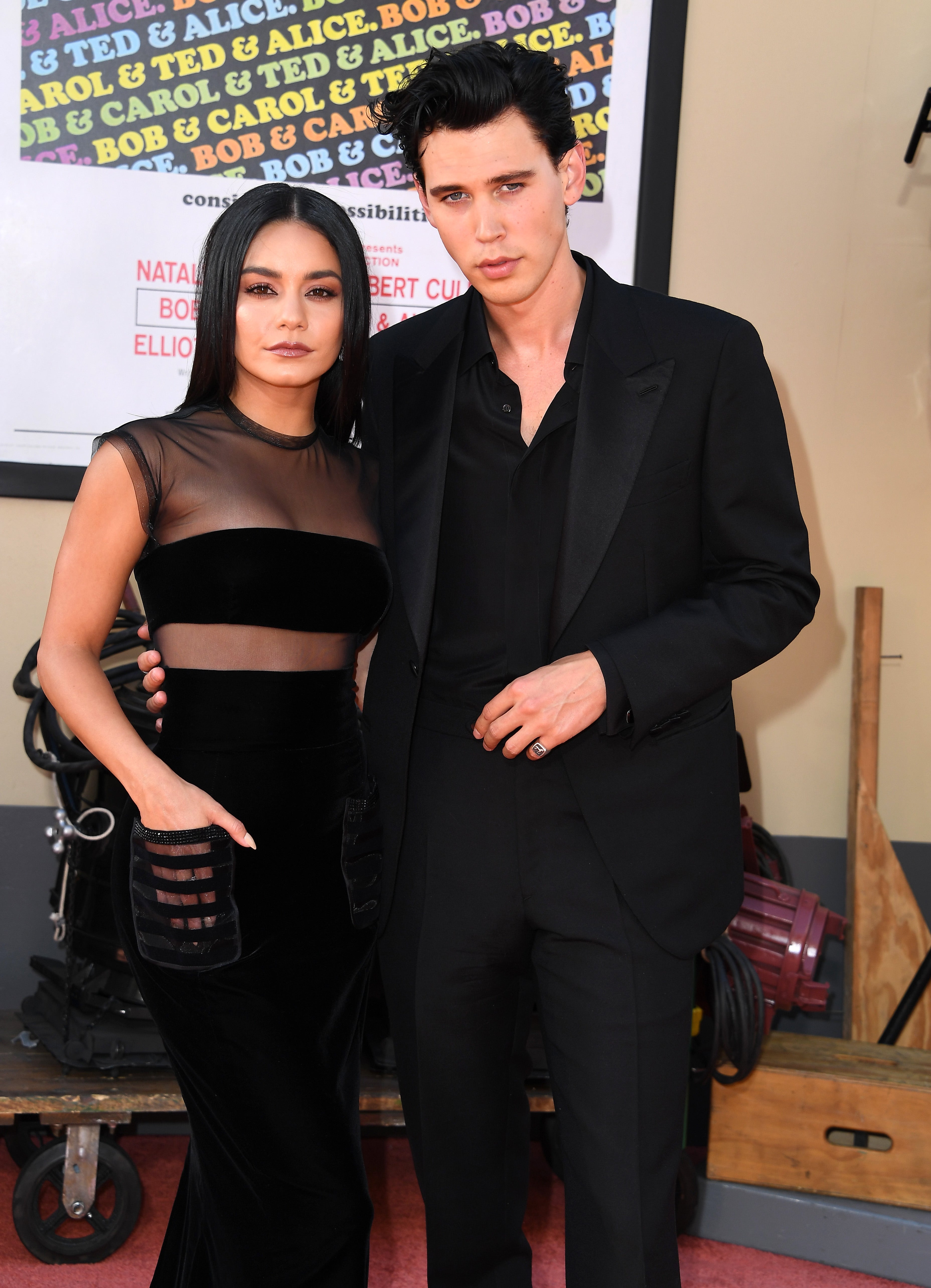 To personer i elegante svarte antrekk på en rød løper; den ene iført en ren topp, den andre en klassisk dress