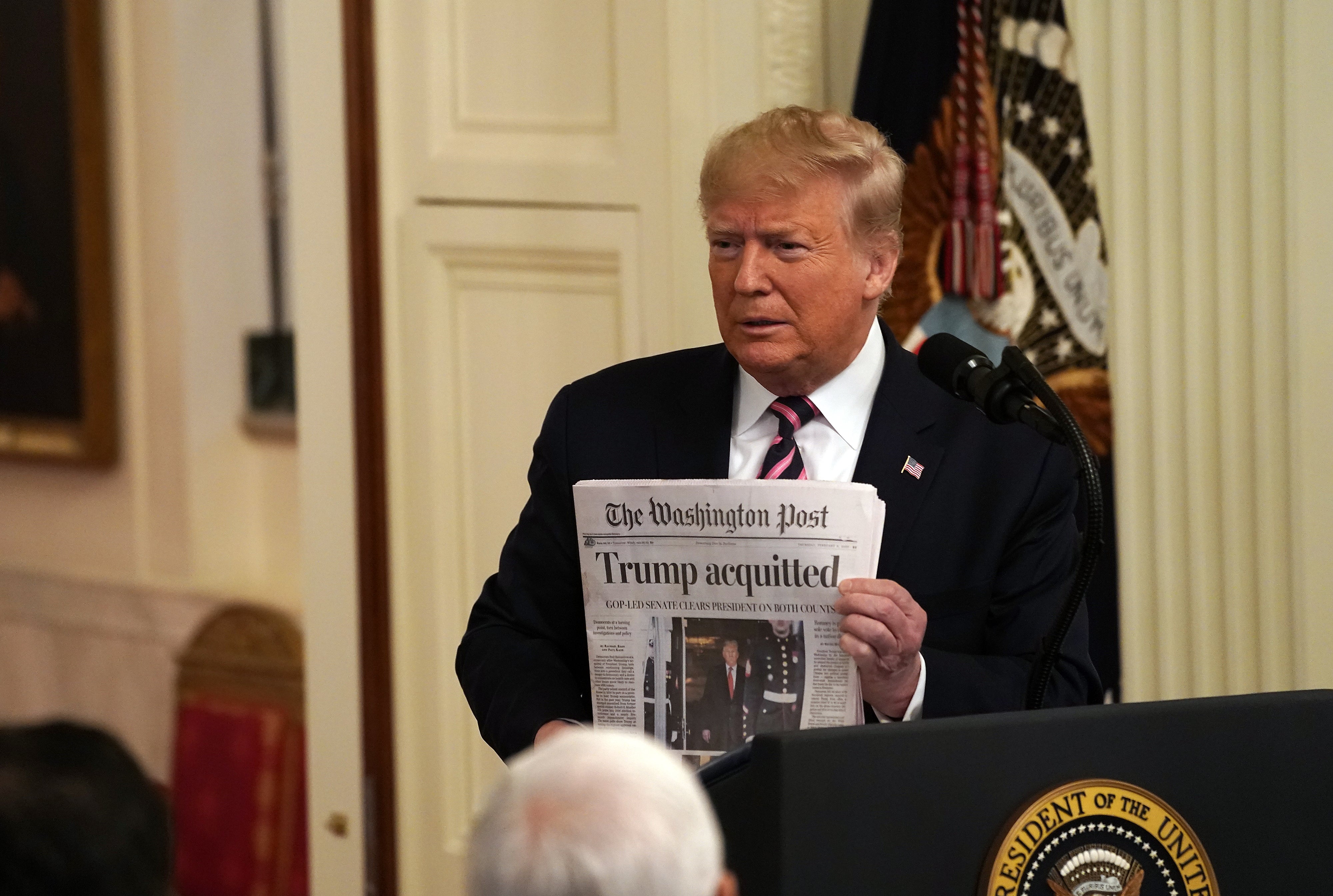 Mann i dress holder en avis med overskriften 