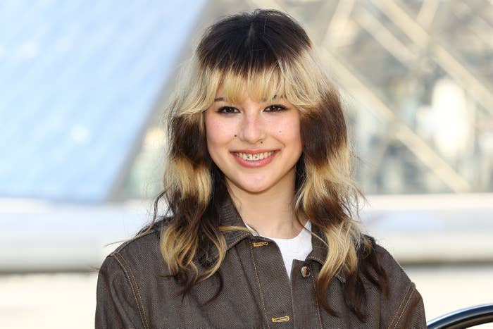 Person with layered hairstyle wearing a casual jacket, smiling outdoors