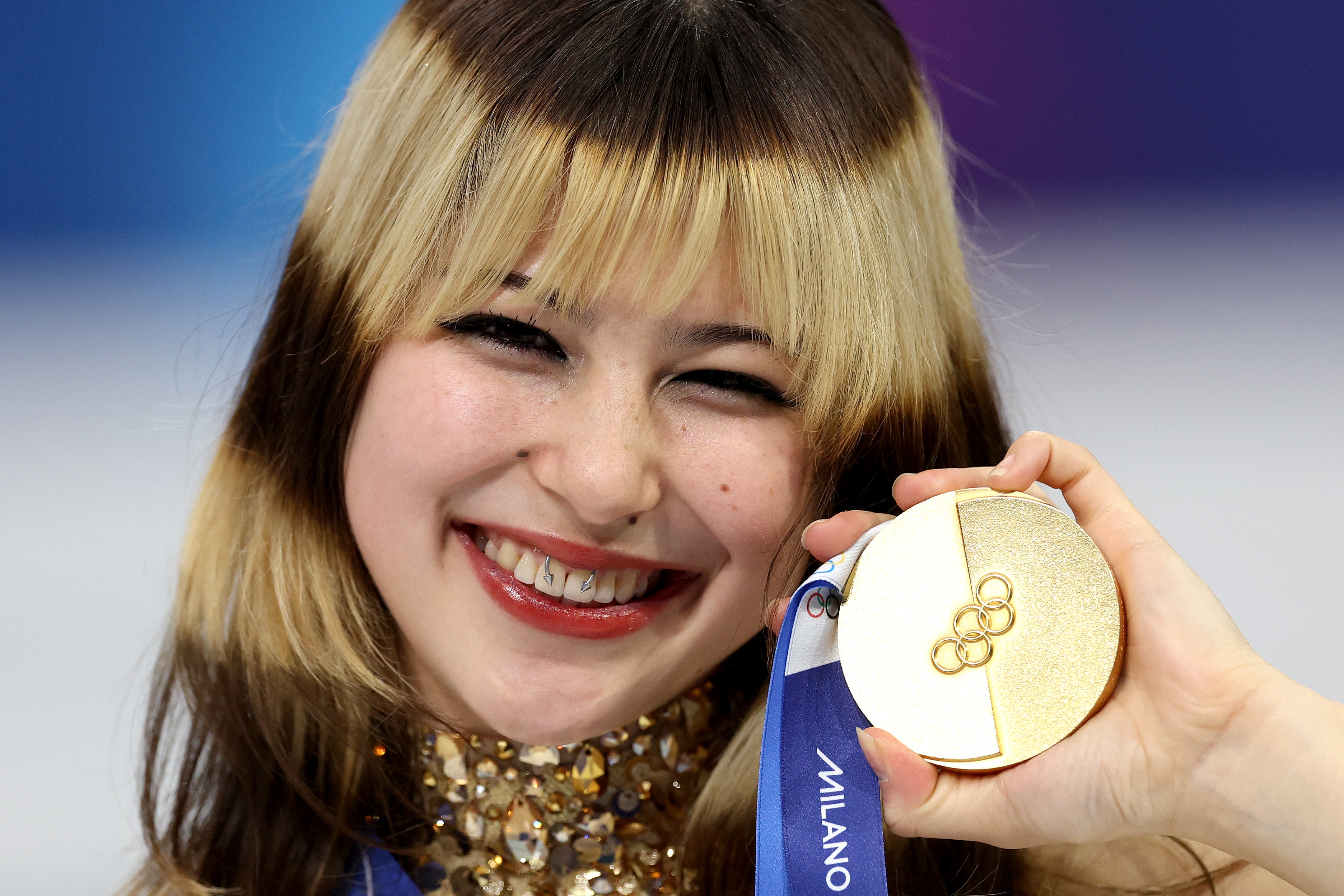 Celebrity holding a golden  medal, smiling, wearing a sequined outfit