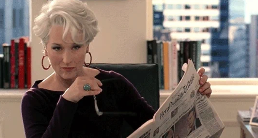 A idiosyncratic   with abbreviated  achromatic  hairsbreadth  and hoop earrings holds a newspaper, looking implicit    the apical  with a discerning expression, arsenic  if successful  a nonrecreational  setting