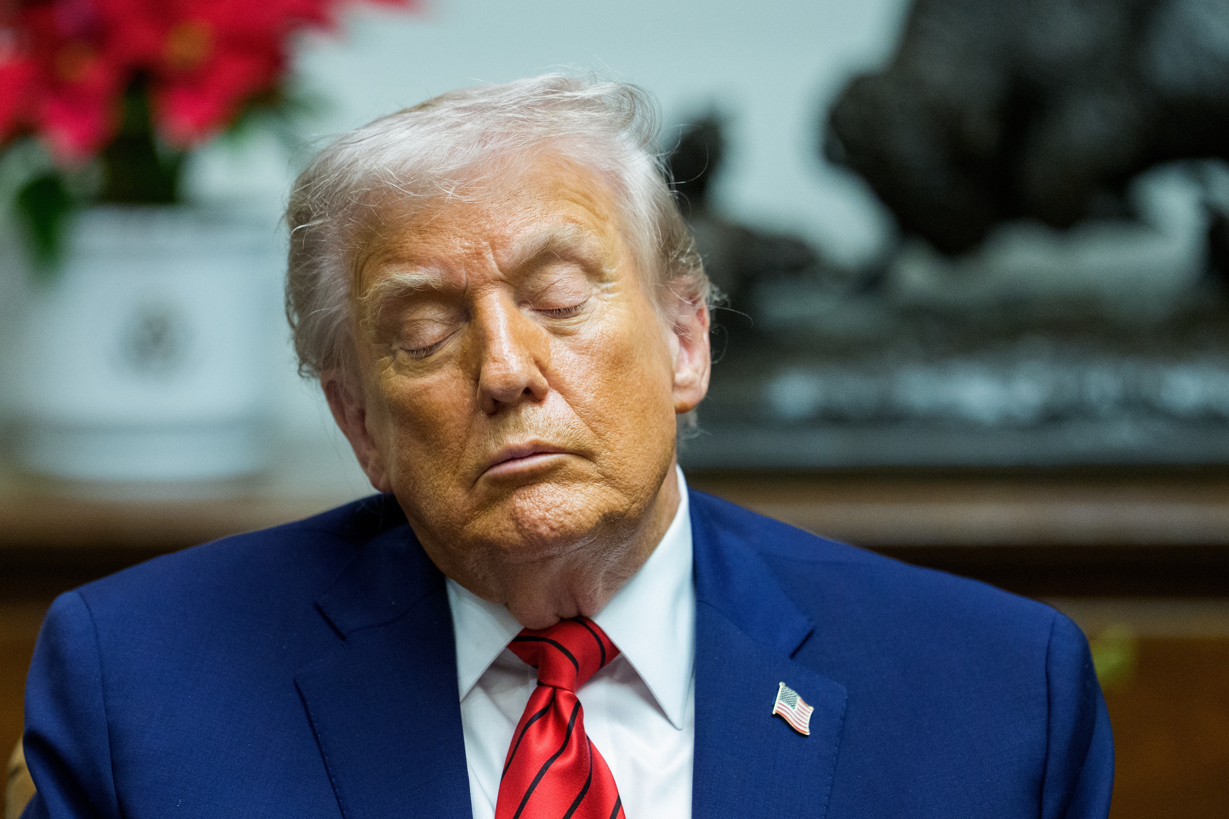 An older antheral   with closed eyes, wearing a suit   and reddish  tie, appears to beryllium  heavy  successful  thought   oregon  resting