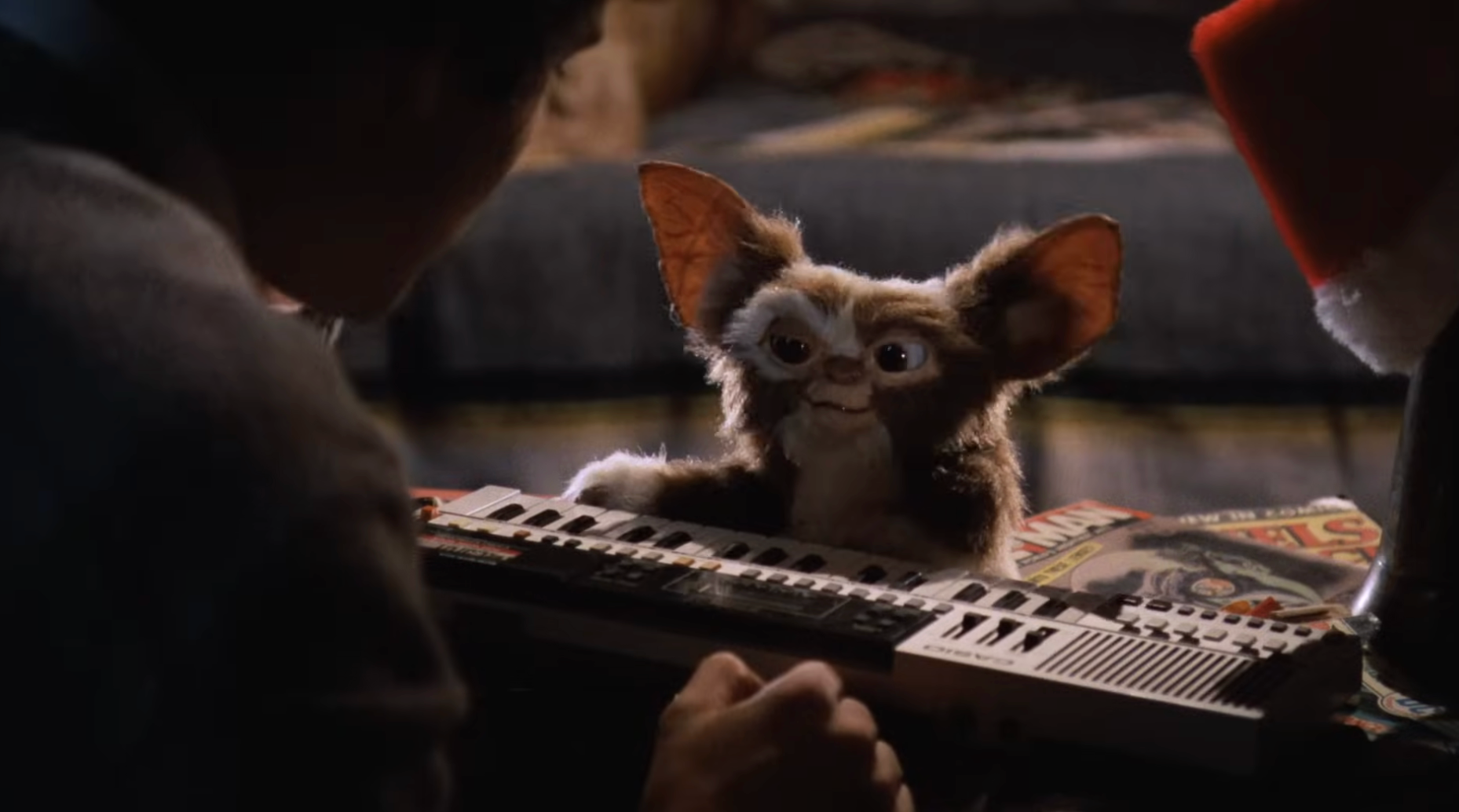 A Gremlin sits connected  a array  adjacent  to magazines, facing idiosyncratic    playing a keyboard, successful  a cozy indoor setting