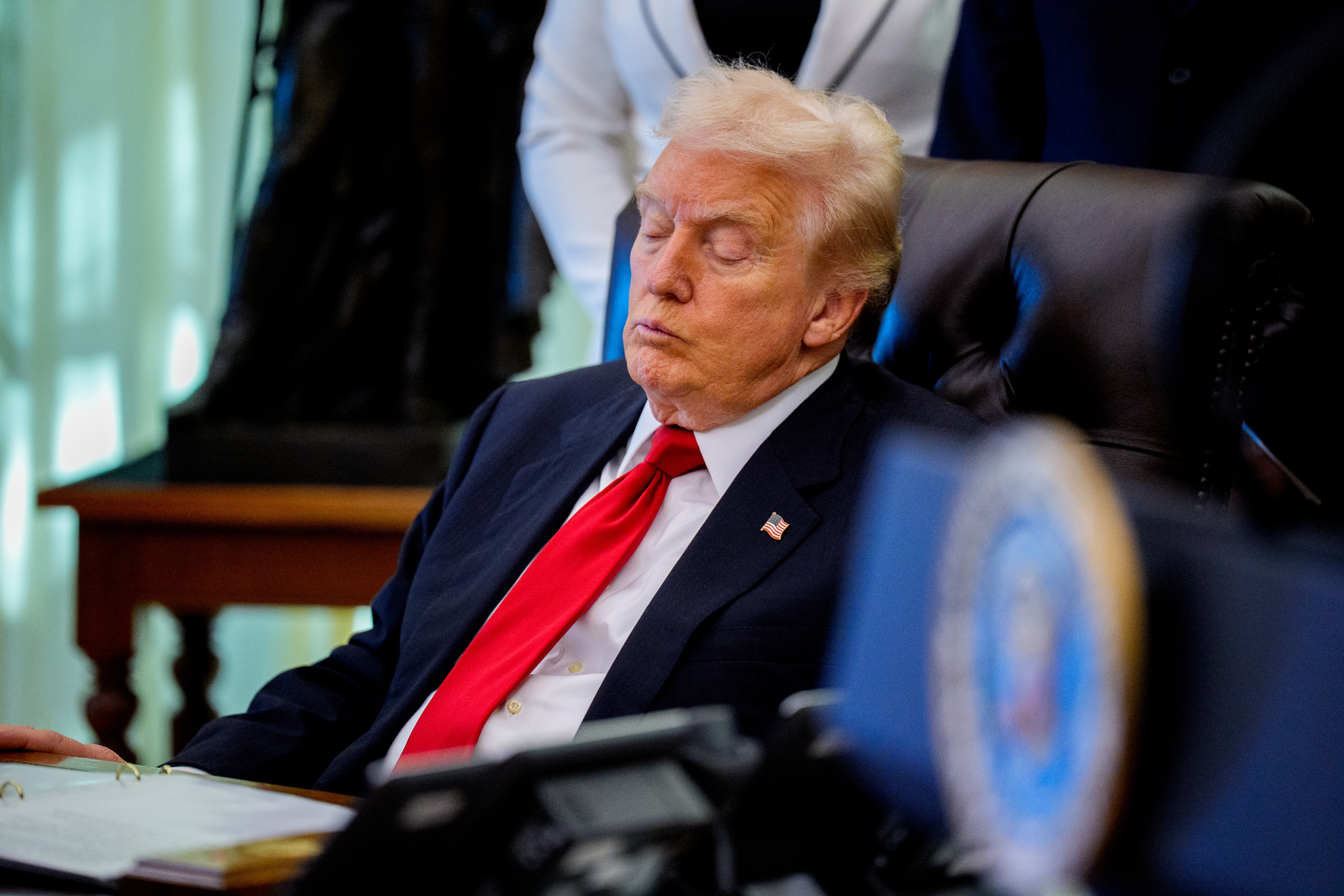 Person successful  suit   with reddish  necktie  sitting astatine  a desk, appearing to beryllium  dormant  oregon  resting, successful  a ceremonial  bureau   setting