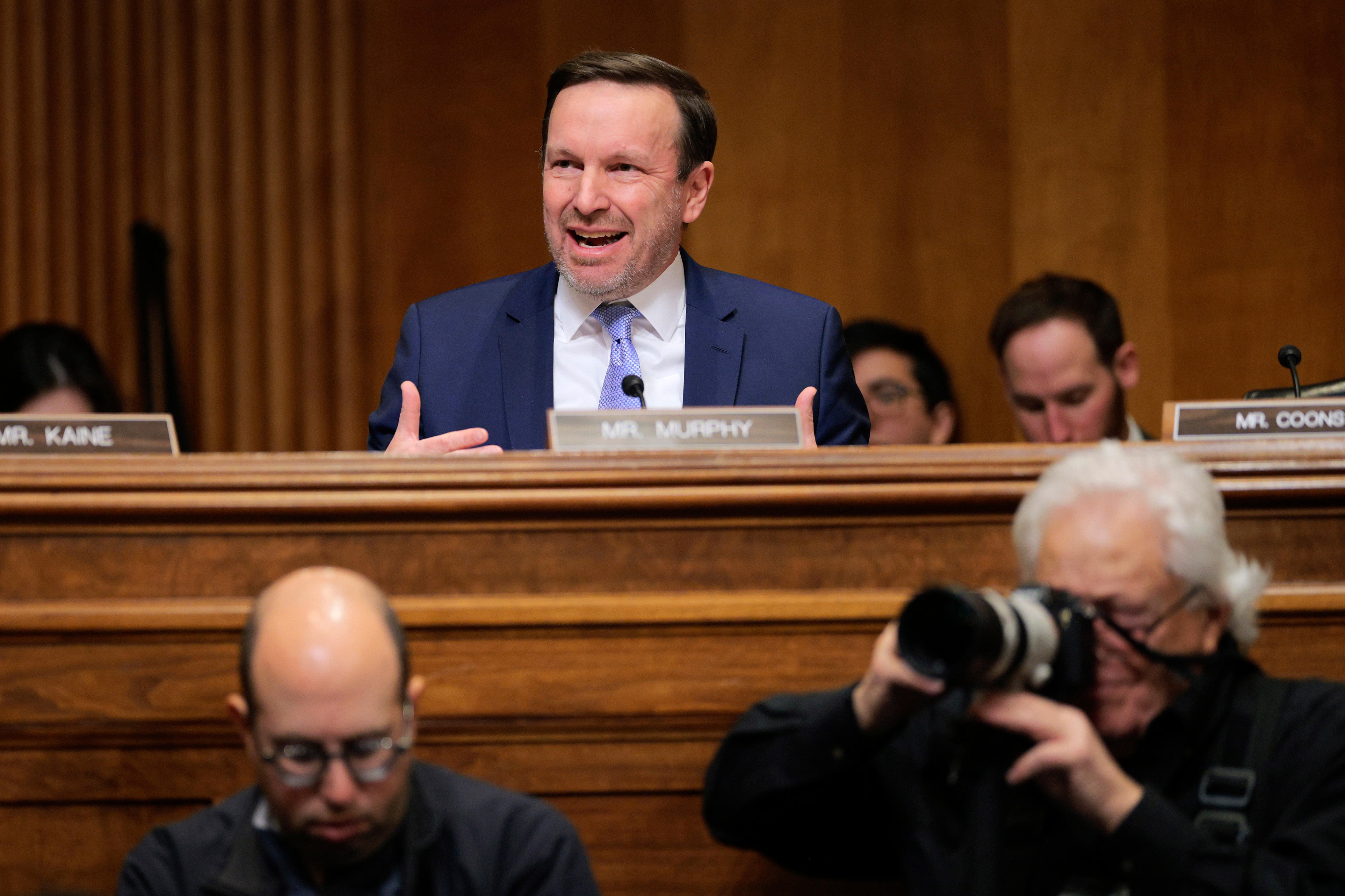 A antheral   successful  ceremonial  attire speaks passionately astatine  a Senate panel. Photographers and attendees are disposable   successful  the foreground