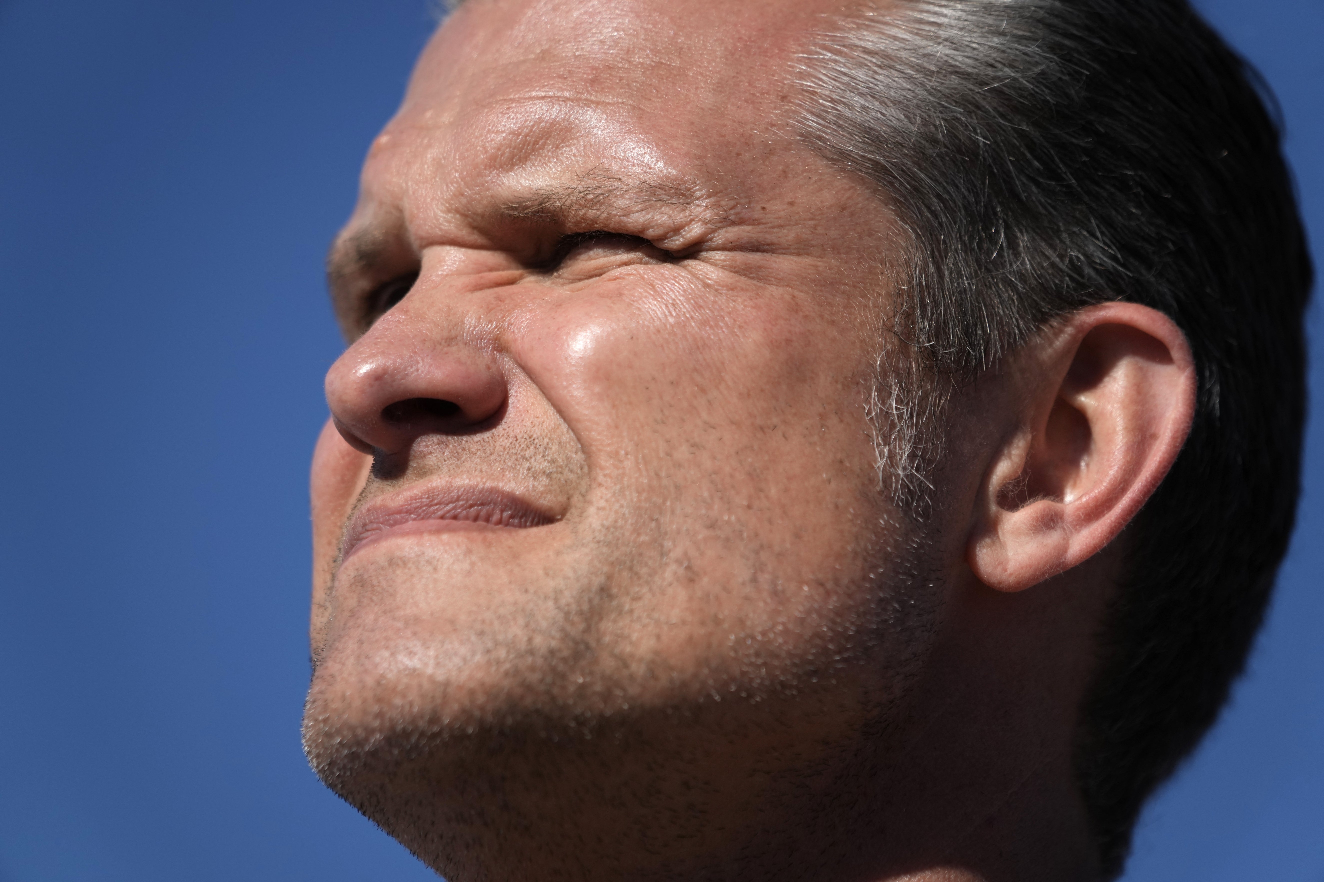 Pete Hegseth myser dramatisk med en knallblå himmel bak seg