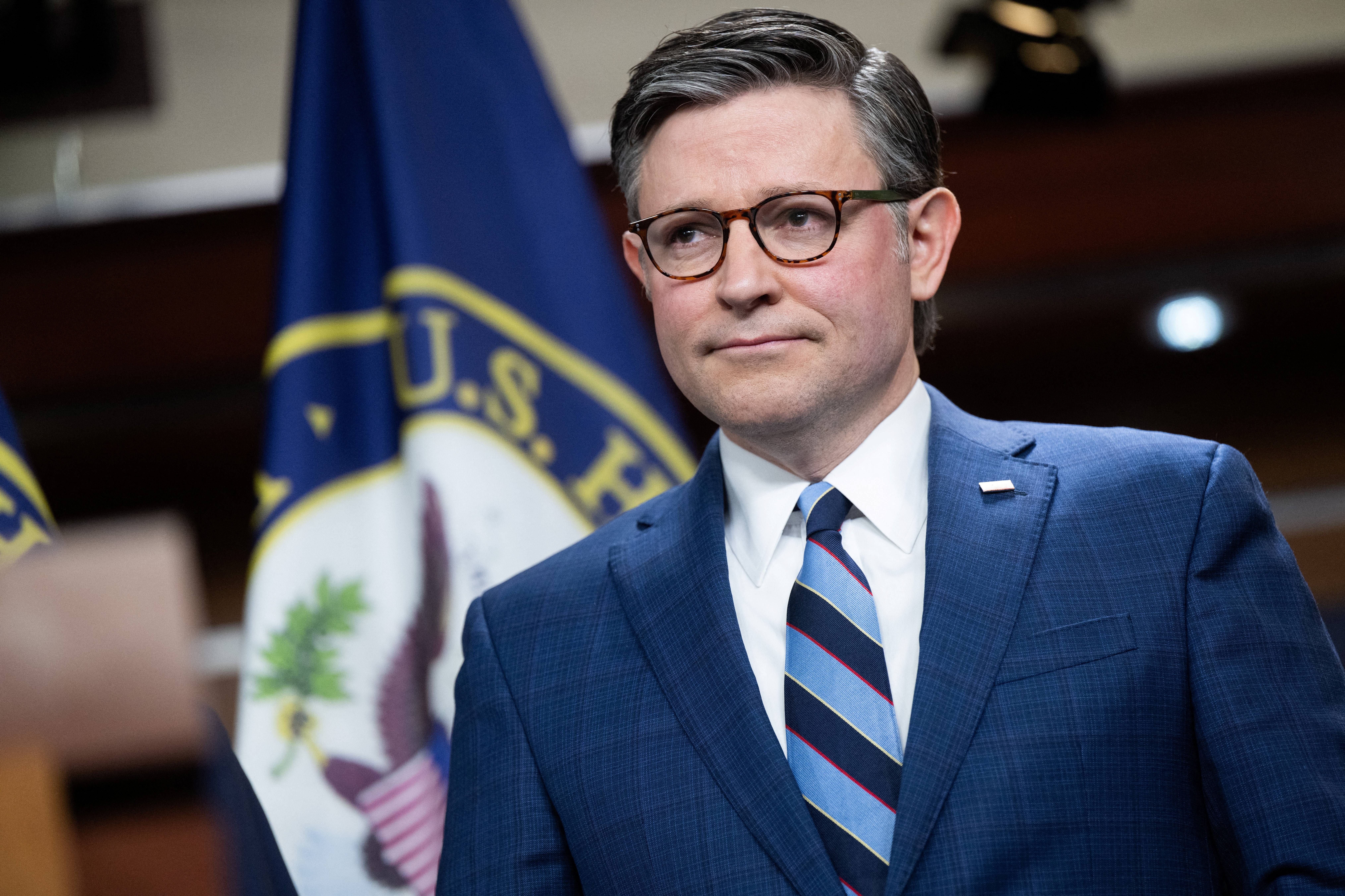 A idiosyncratic   successful  a suit   and striped necktie  stands adjacent   U.S. House flags astatine  a property   event