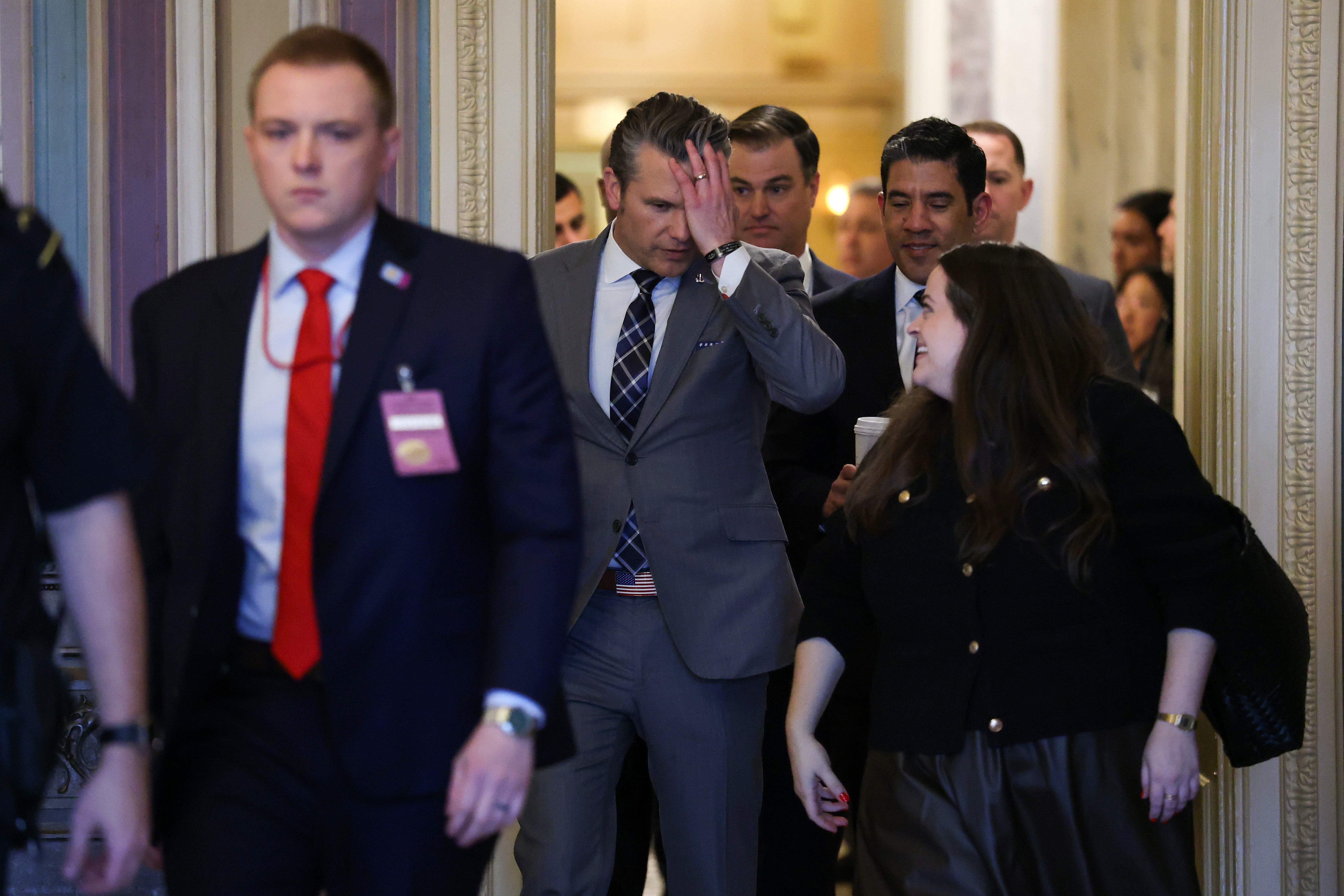 Pete Hegseth med hånden på pannen mens han går sammen med andre i dress med merkelapper rundt halsen