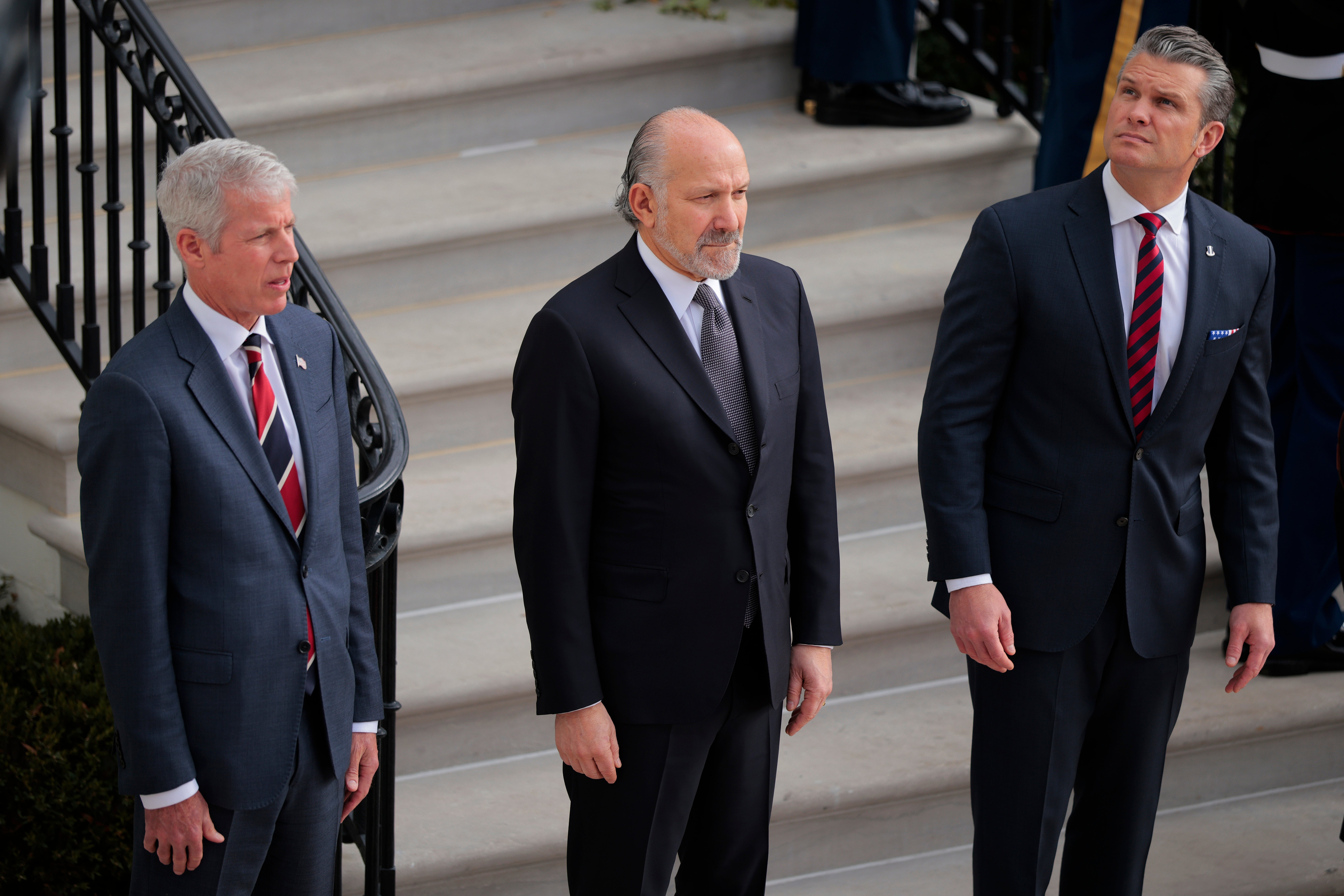 Chris Wright, Howard Lutnick og Pete Hegseth står på trappen til Det hvite hus; Hegseth ser bekymret mot himmelen