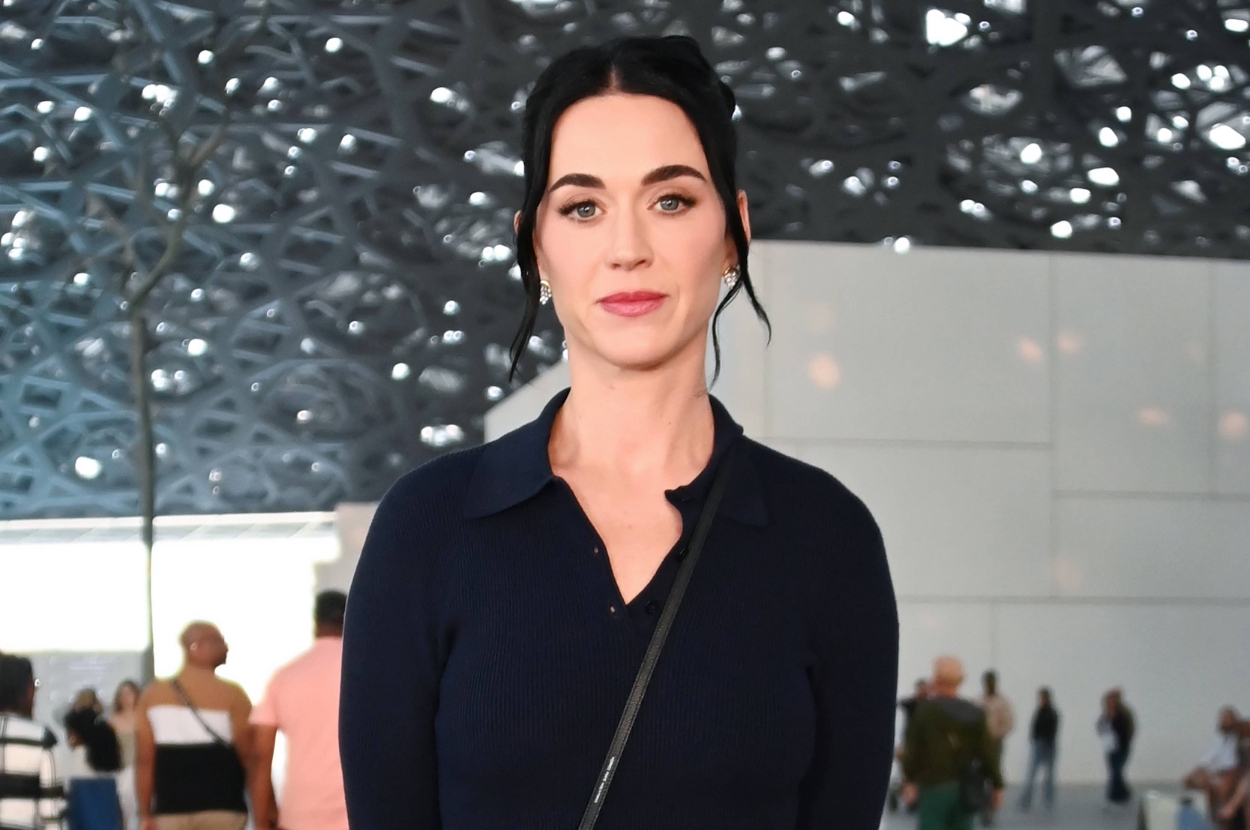 A person in a stylish dark top with a crossbody bag stands indoors at an event. People are visible in the background