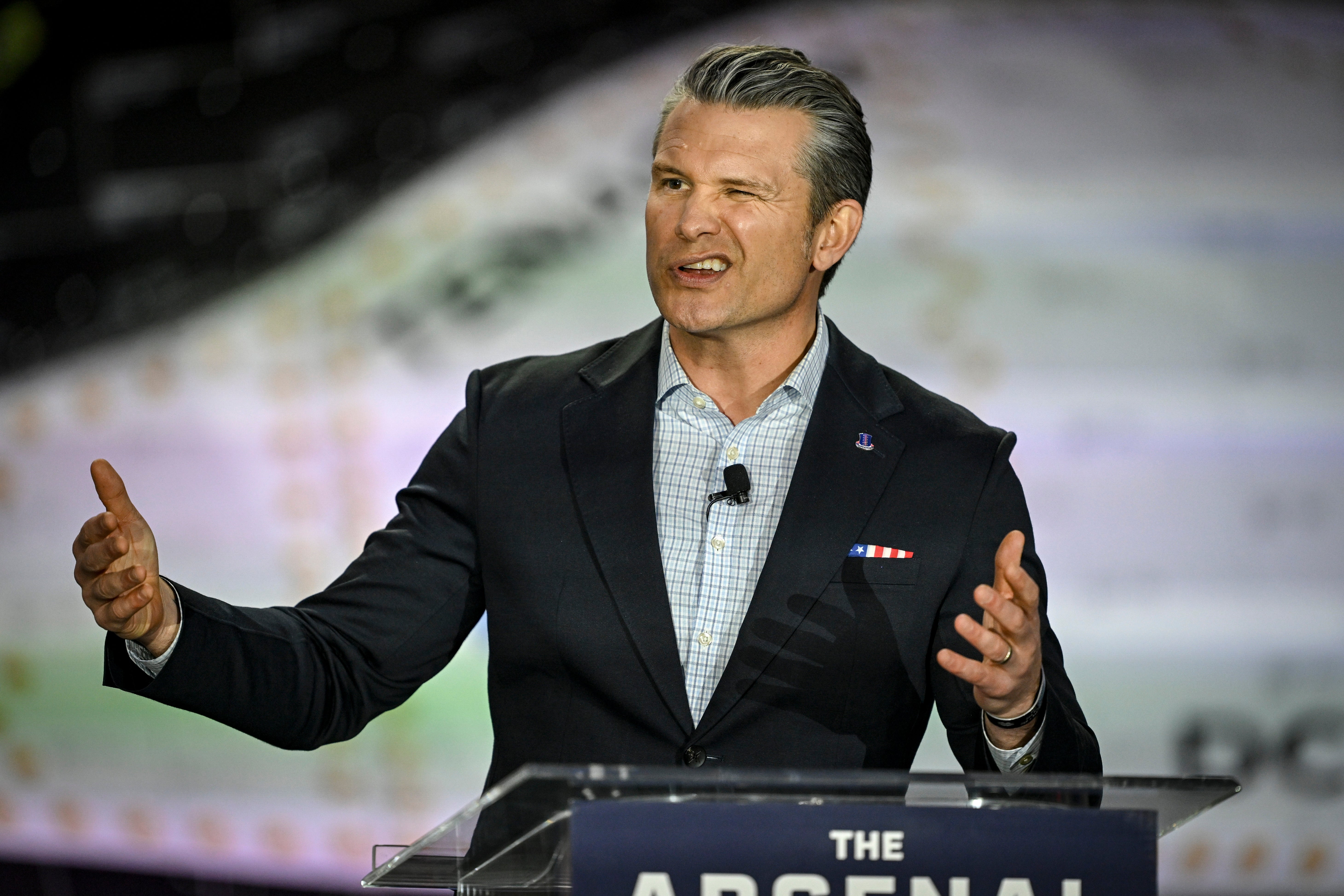 Pete Hegseth snakker ved et podium og blunker med den ene siden av munnen hevet