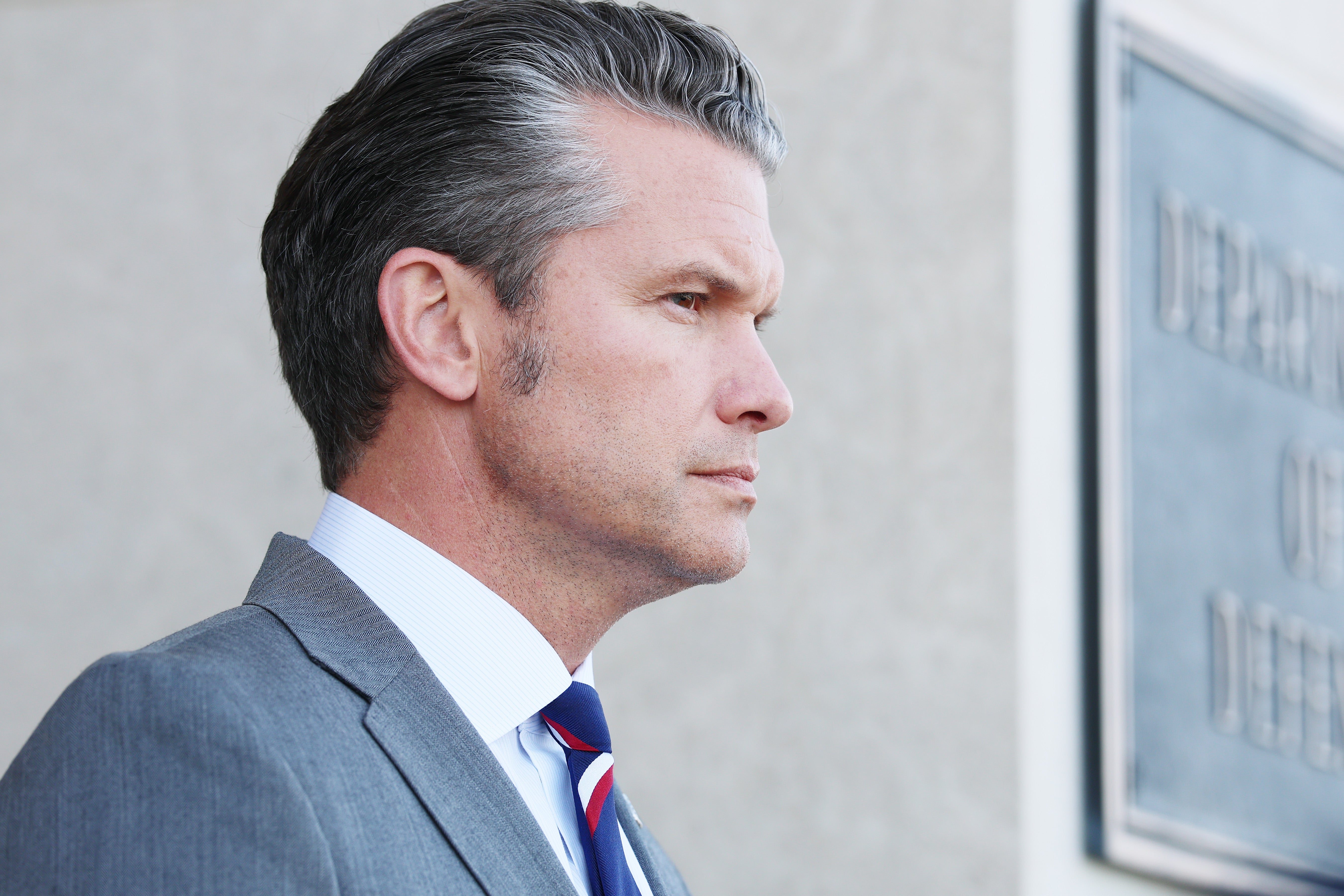 Pete Hegseth i dress med stripet slips står i profil utenfor et regjeringsbygg