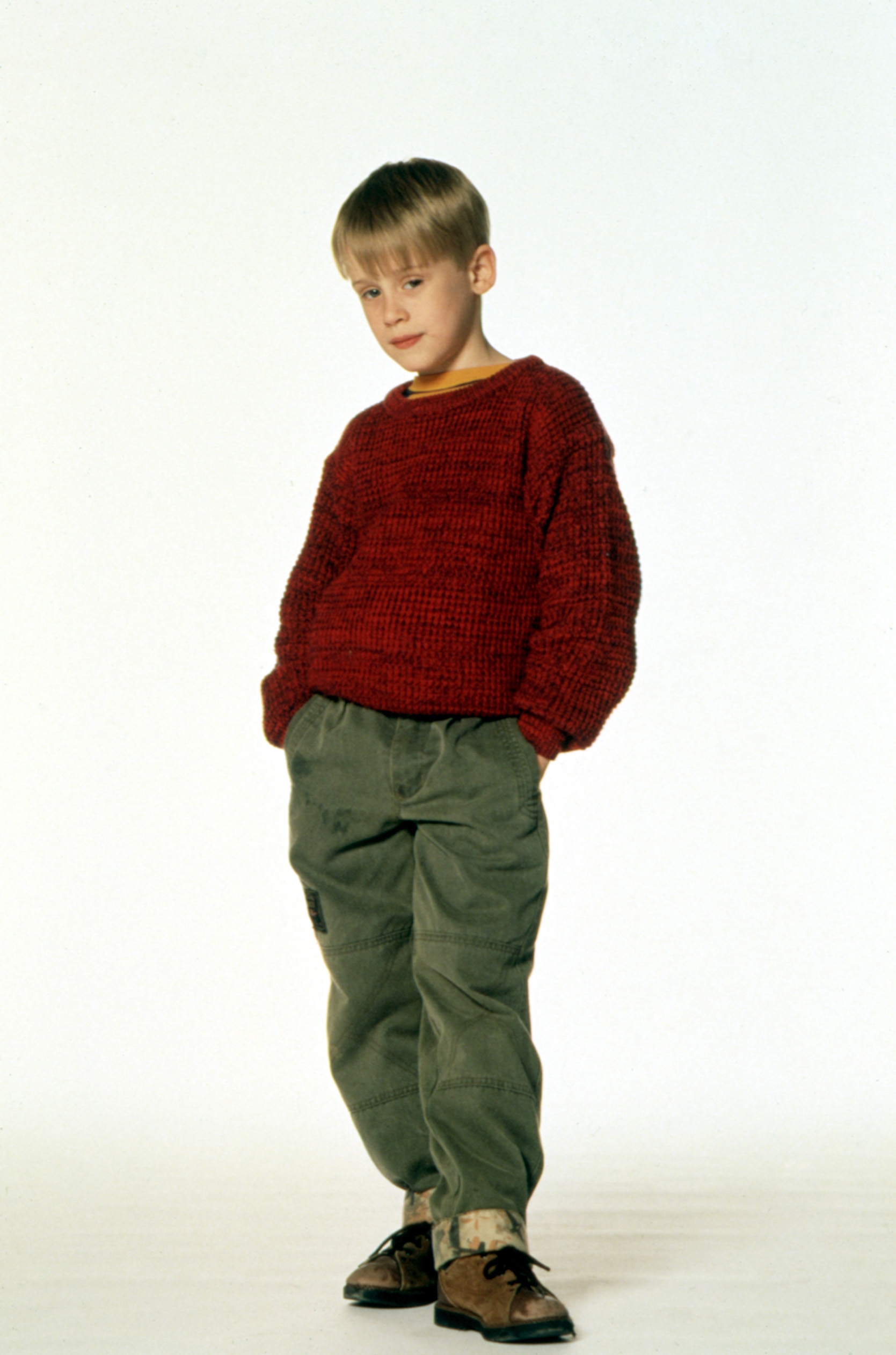 Child histrion  poses successful  a sweater and trousers, hands successful  pockets, against a plain backdrop