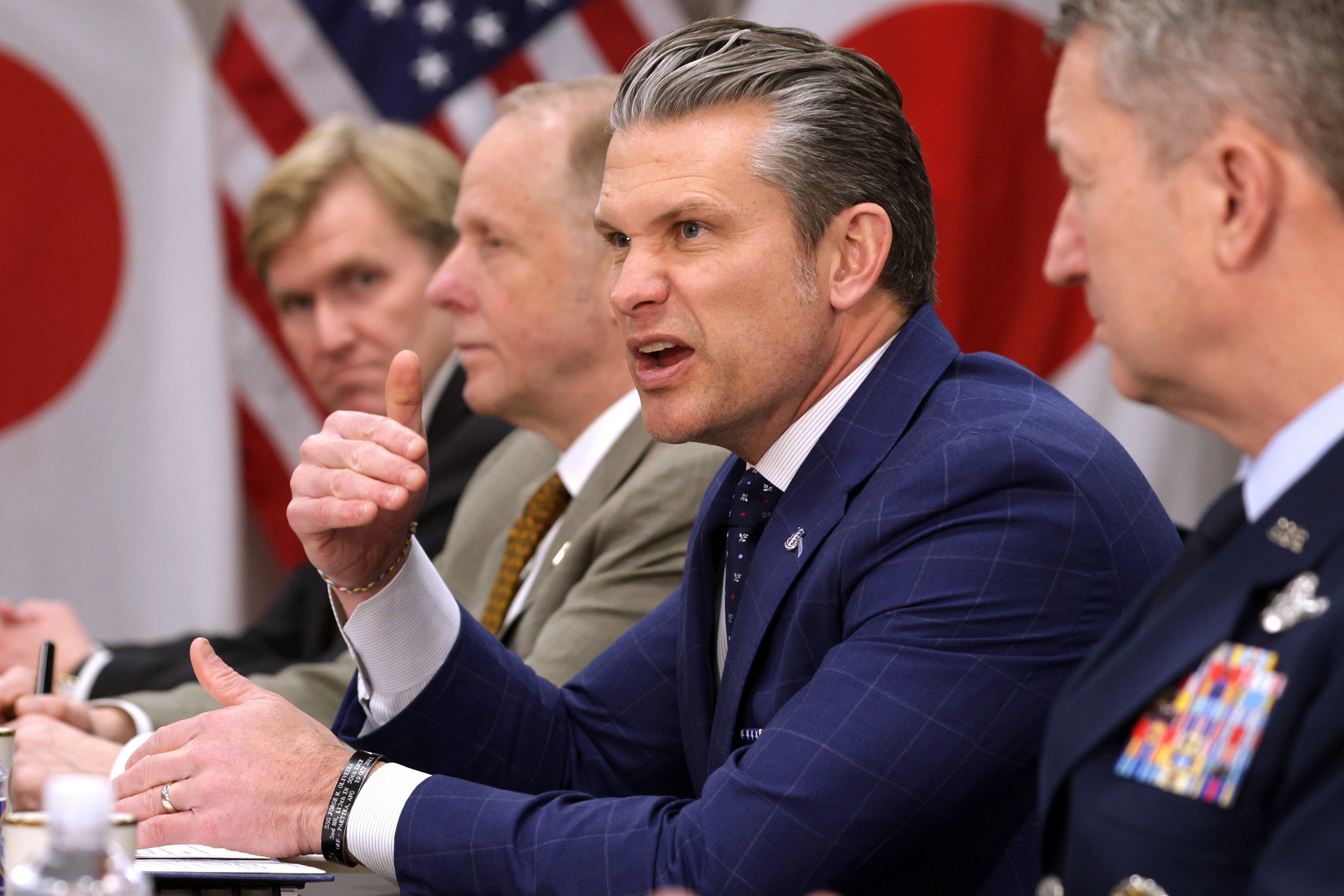En gruppe tjenestemenn i dress og militærantrekk ved et konferansebord taler, med flagg fra Japan og USA i bakgrunnen. Pete Hegseth står i sentrum og gestikulerer med et sint ansiktsuttrykk