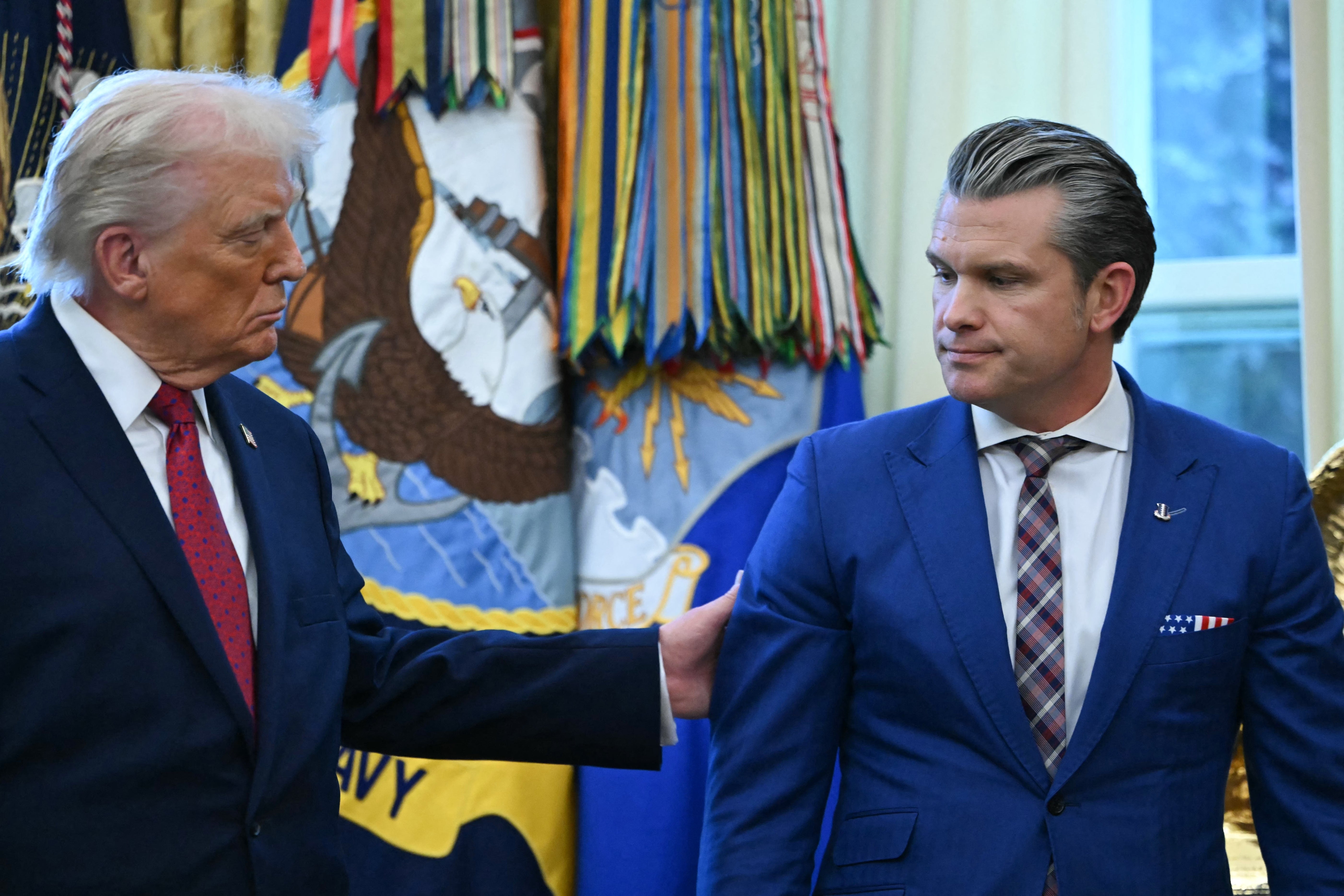 Donald Trump og Pete Hegseth på det ovale kontoret; Trump griper Hegseth i høyre overarm for å trekke ham et sted