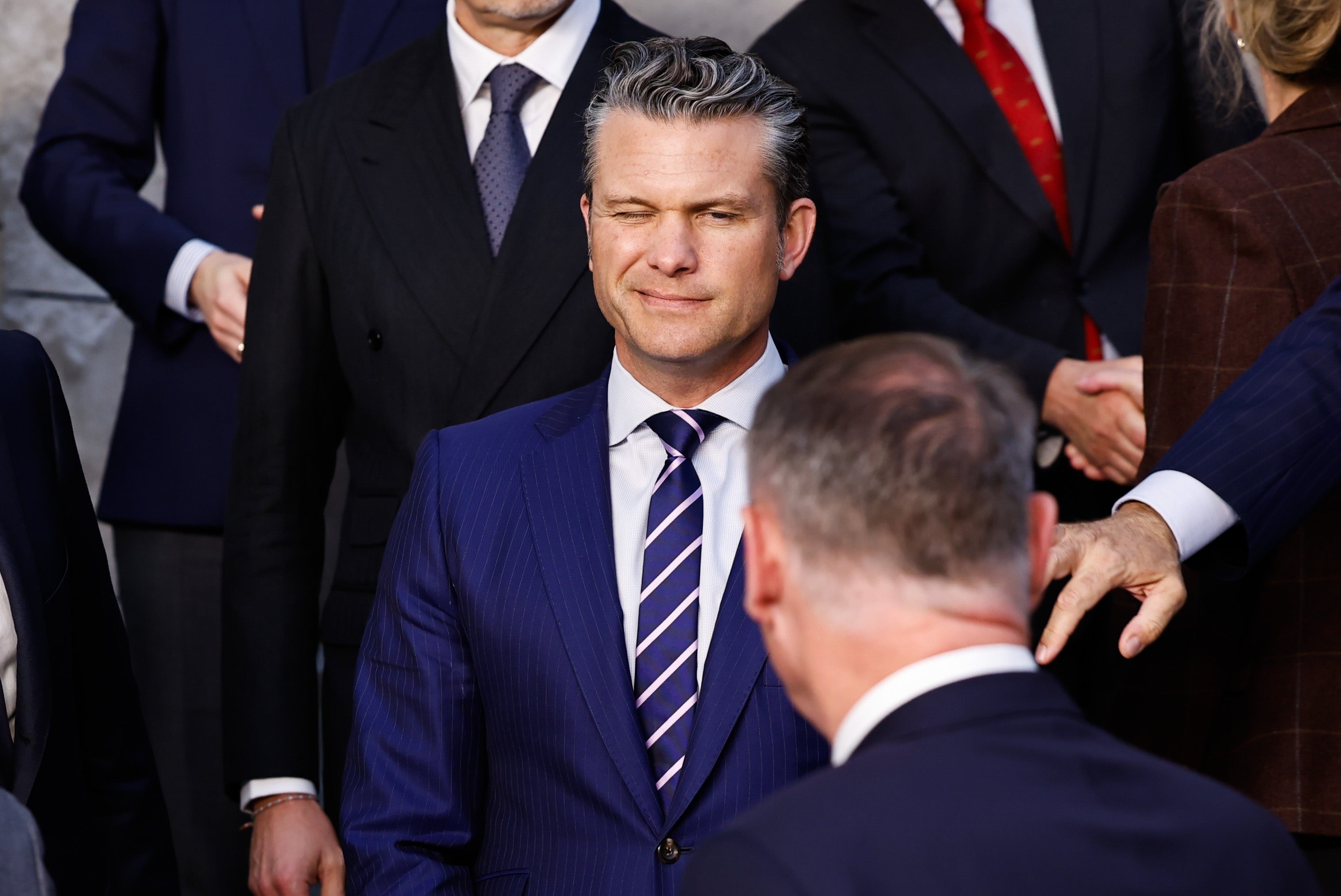 Pete Hegseth blant et hav av dresser, gir noen et blunk, men begge øynene hans er stort sett lukket