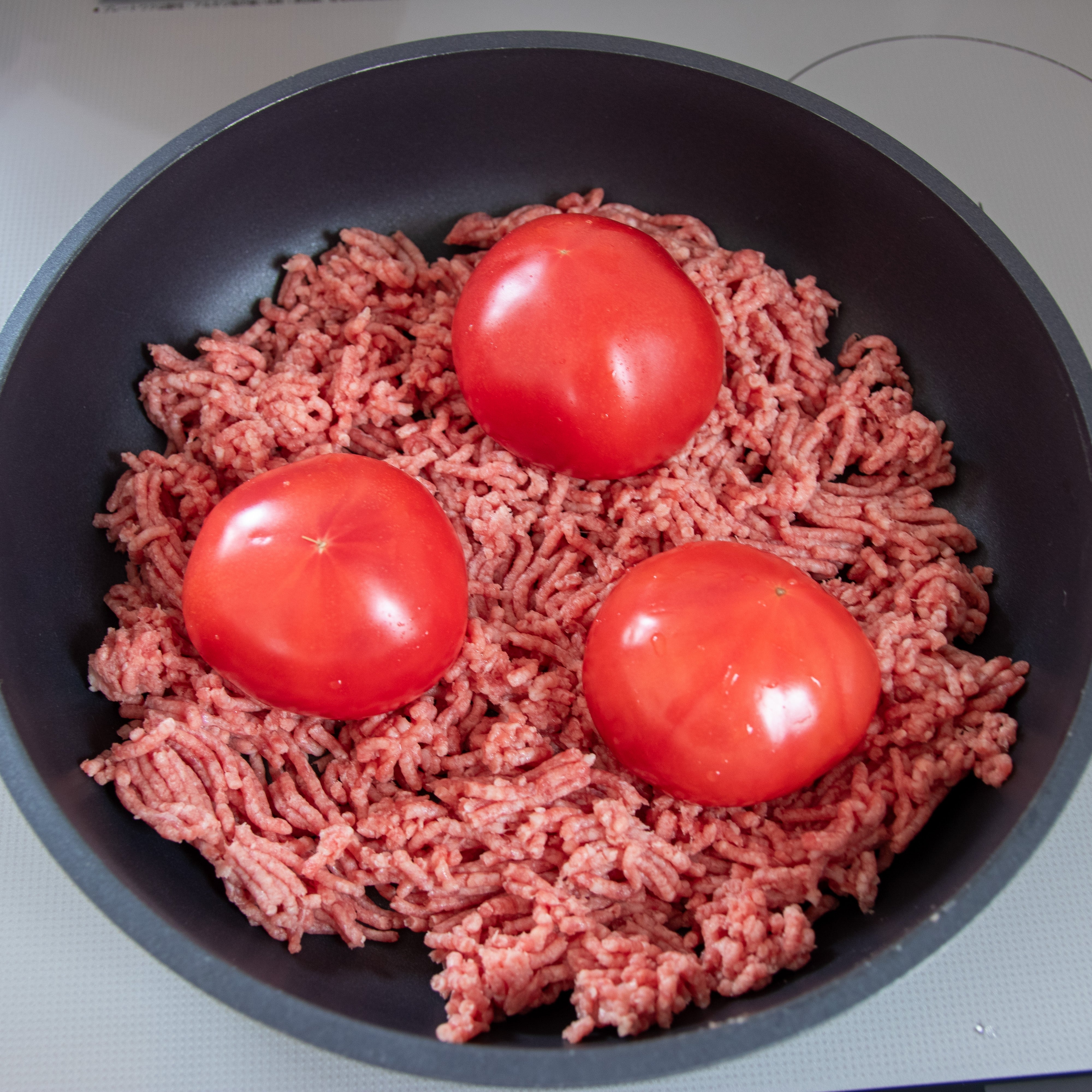 フライパンにひき肉とトマト3個が並んでいる。