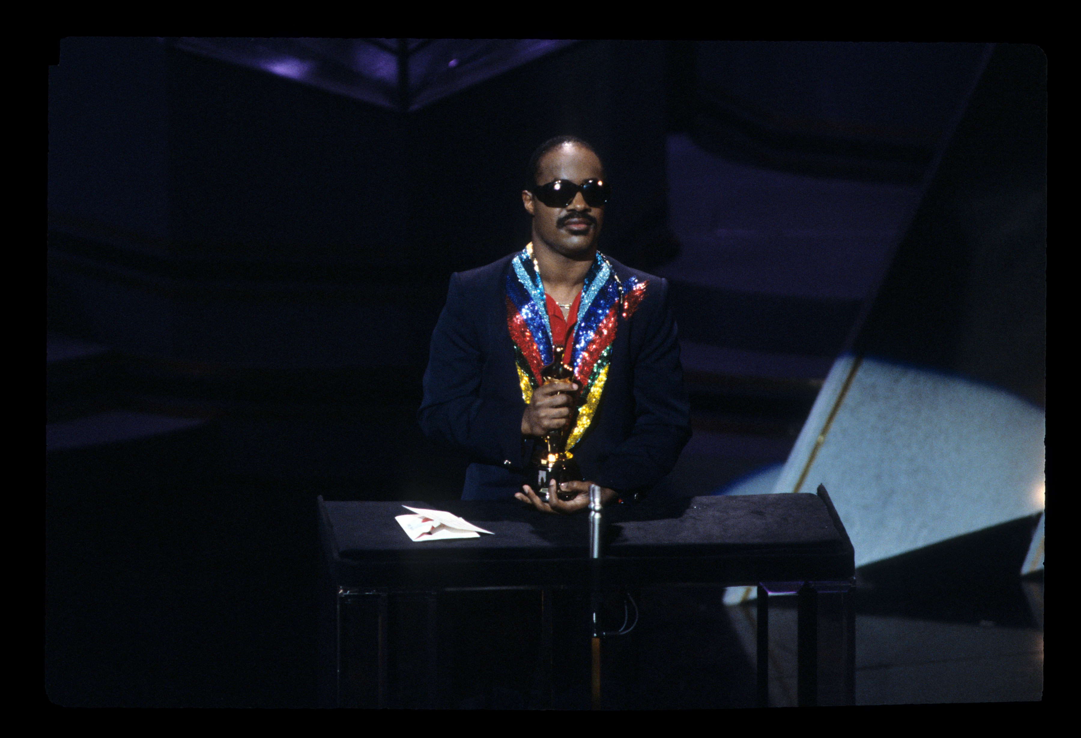 Person connected  signifier    holding a colorful display, wearing sunglasses and a astute  suit, lasting  down  a microphone astatine  an event