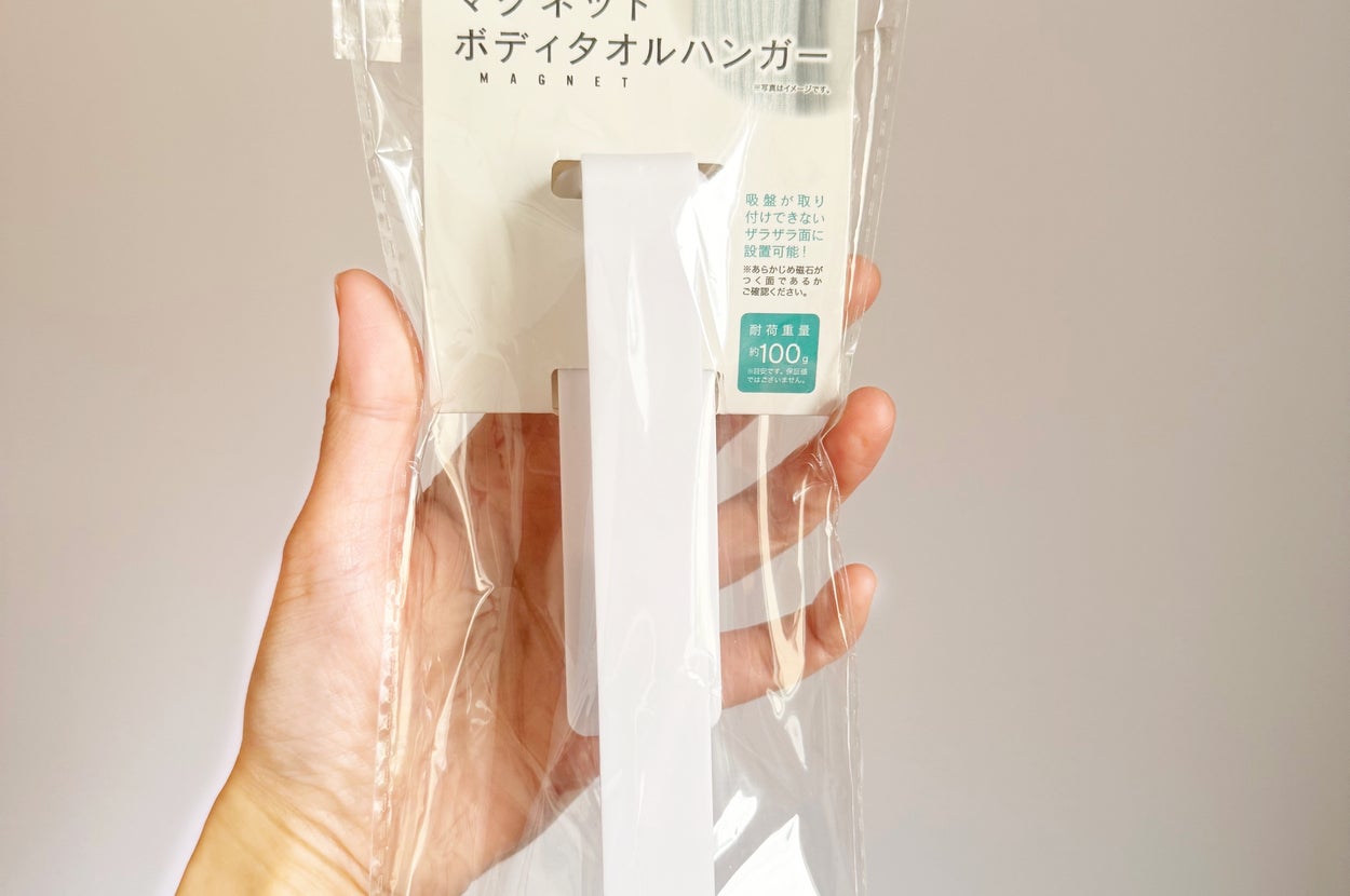 手に持たれたパッケージには、バス用品用の磁石式ボディタオルハンガーが入っています。