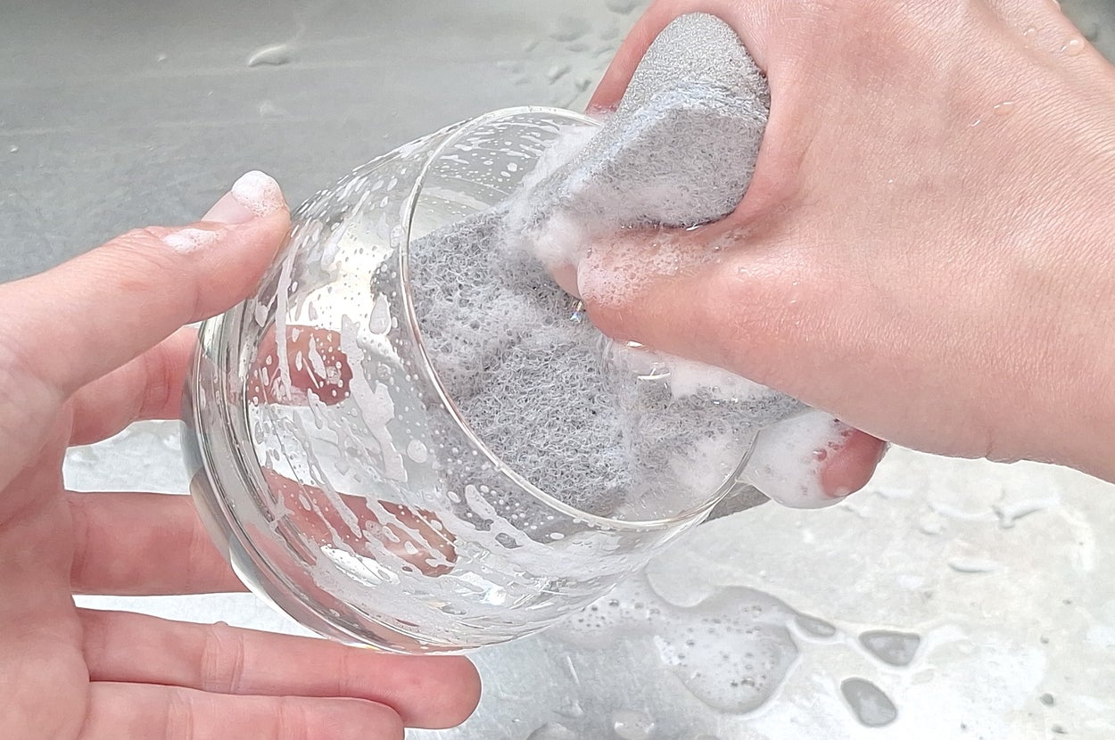 人が泡だらけのスポンジでグラスを洗っています。シンクの上で作業しています。