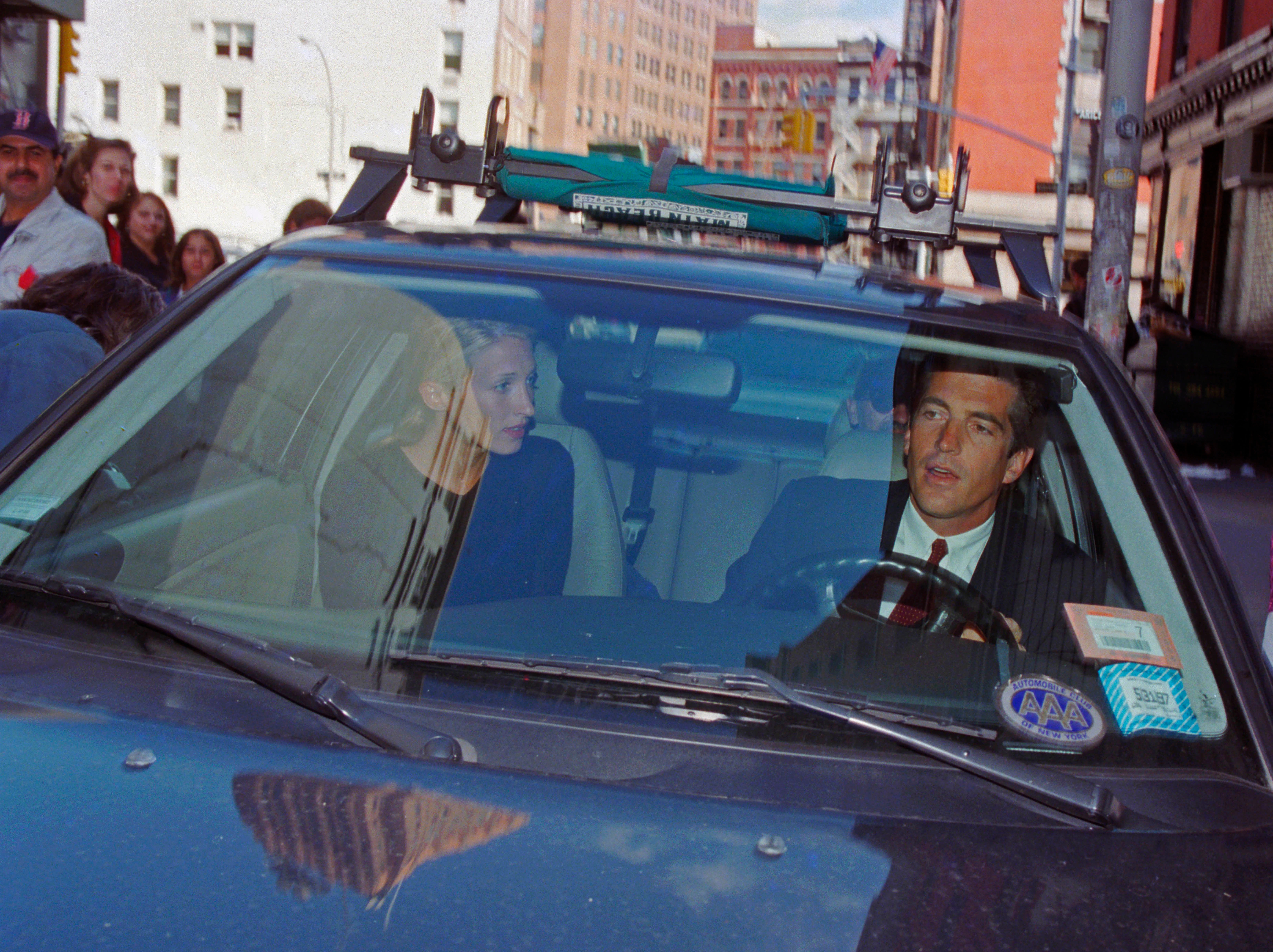 A antheral   and a pistillate   are seen successful  a car   with a metropolis  thoroughfare  successful  the background. The antheral   is driving, and some  look  engaged successful  conversation