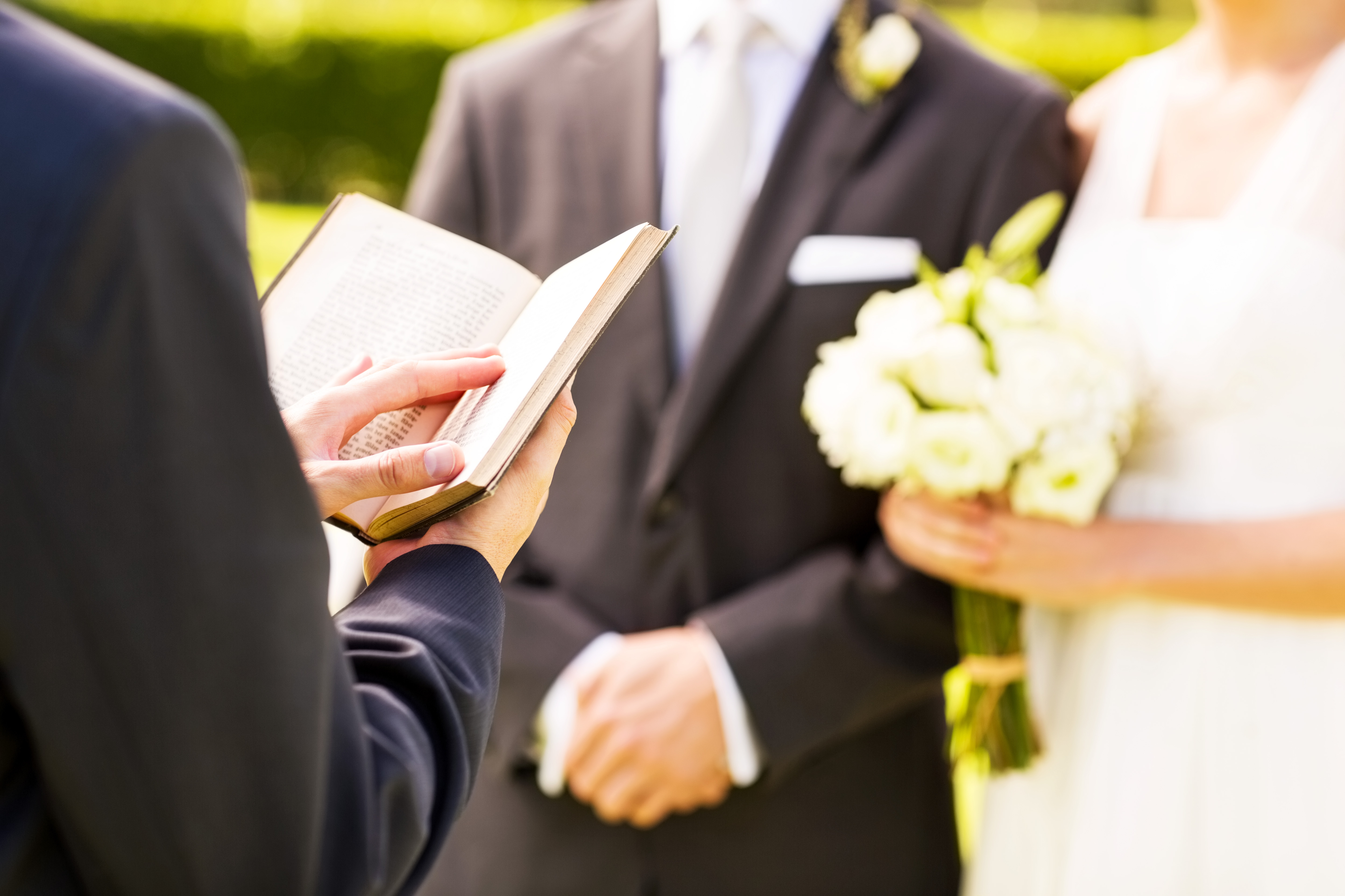 Wedding ceremonial with a mates holding hands, the officiant speechmaking from a book