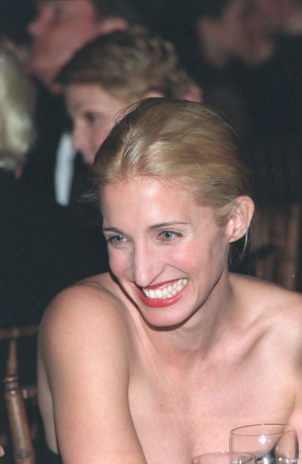 Person smiling astatine  an event, wearing a strapless dress, surrounded by different   guests