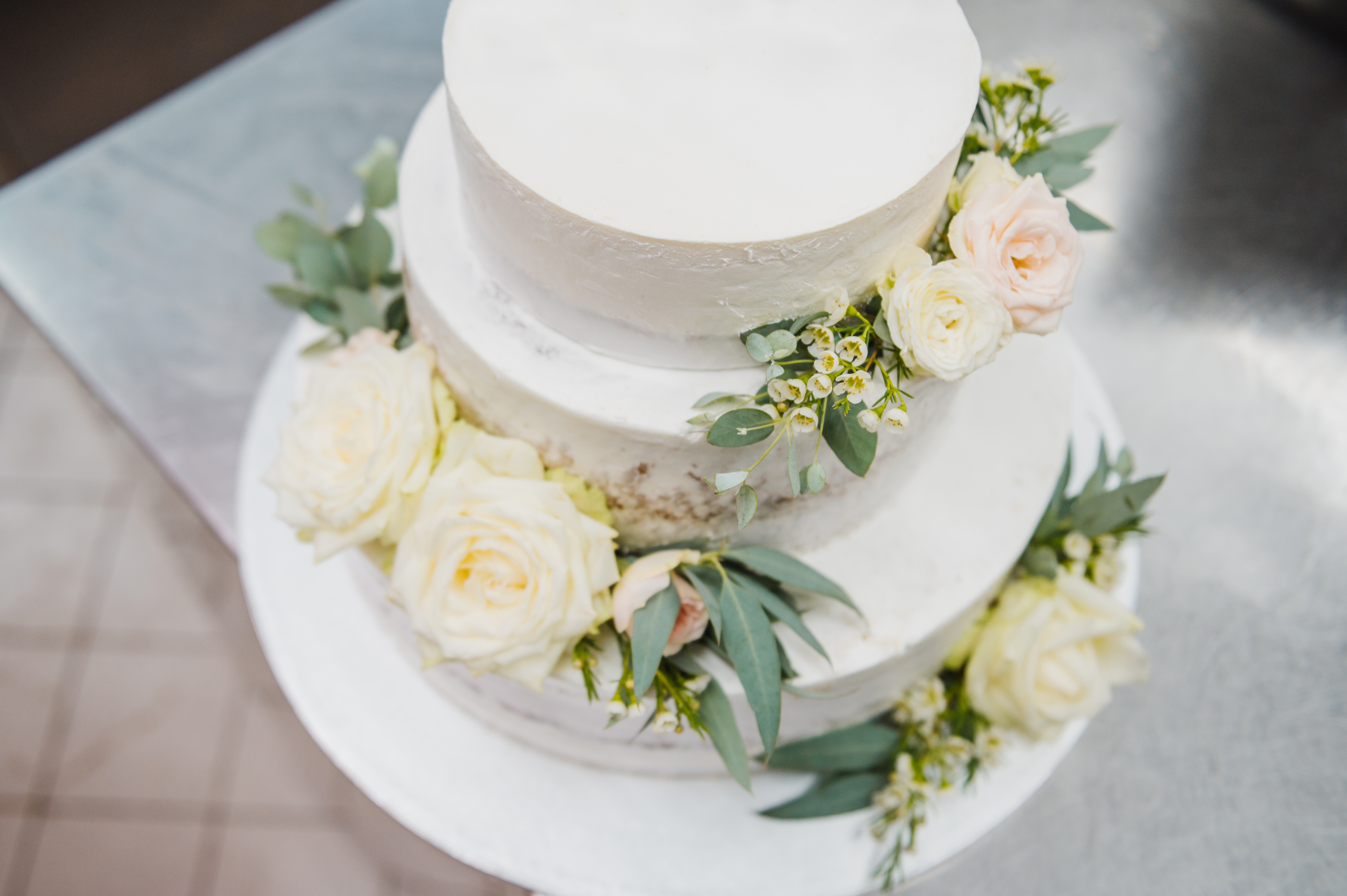 Three-tiered wedding barroom adorned with achromatic roses and greenery