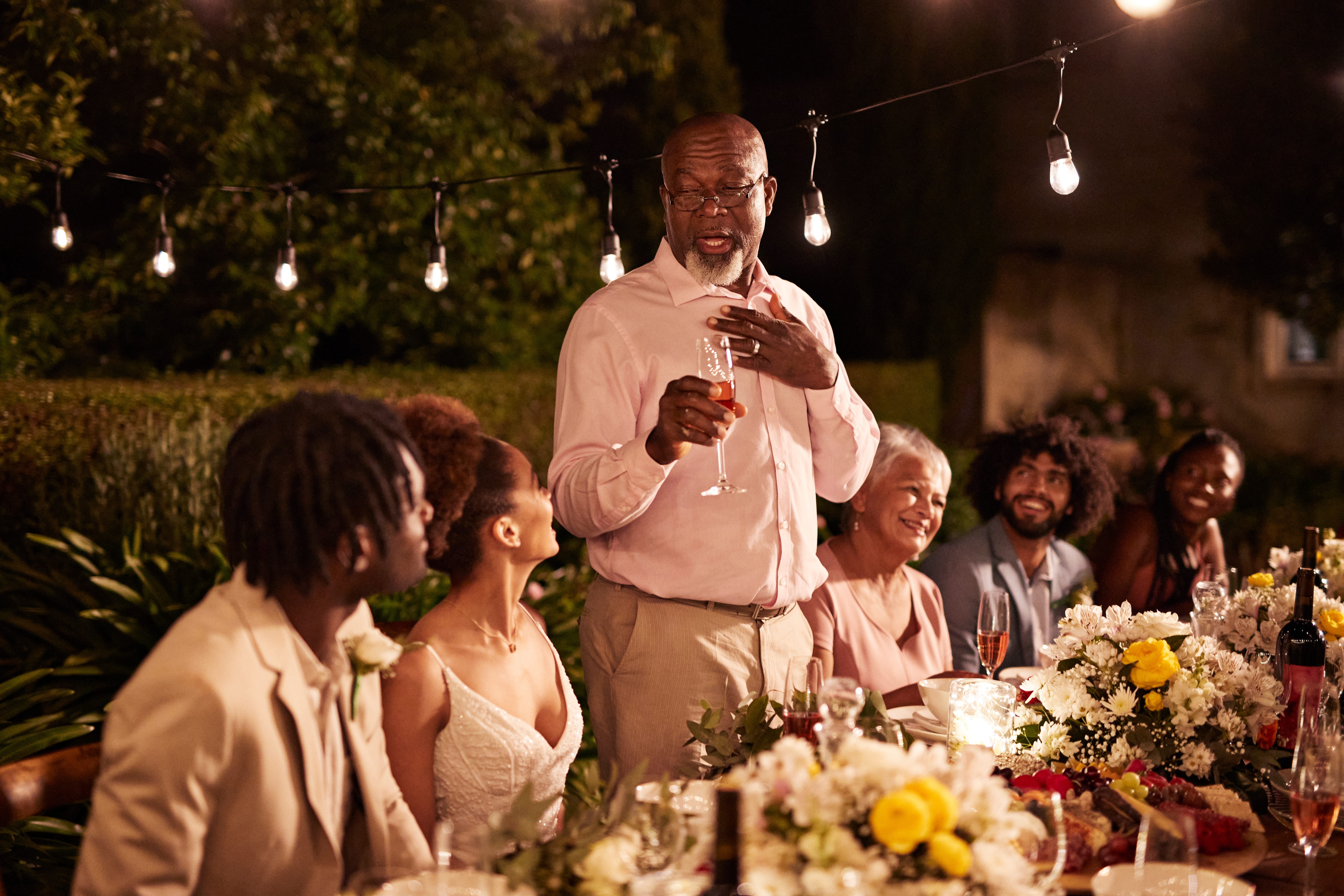 A antheral stands up giving a toast astatine wedding reception with guests gathered astatine a table