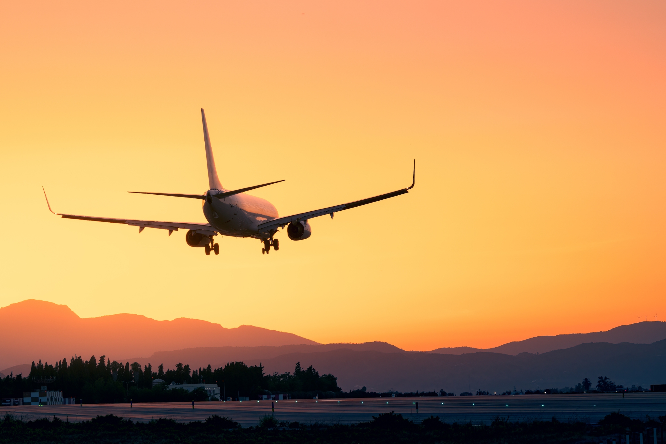 Airplane landing astatine  an airdrome  astatine  sunset, silhouetted against a mountainous horizon