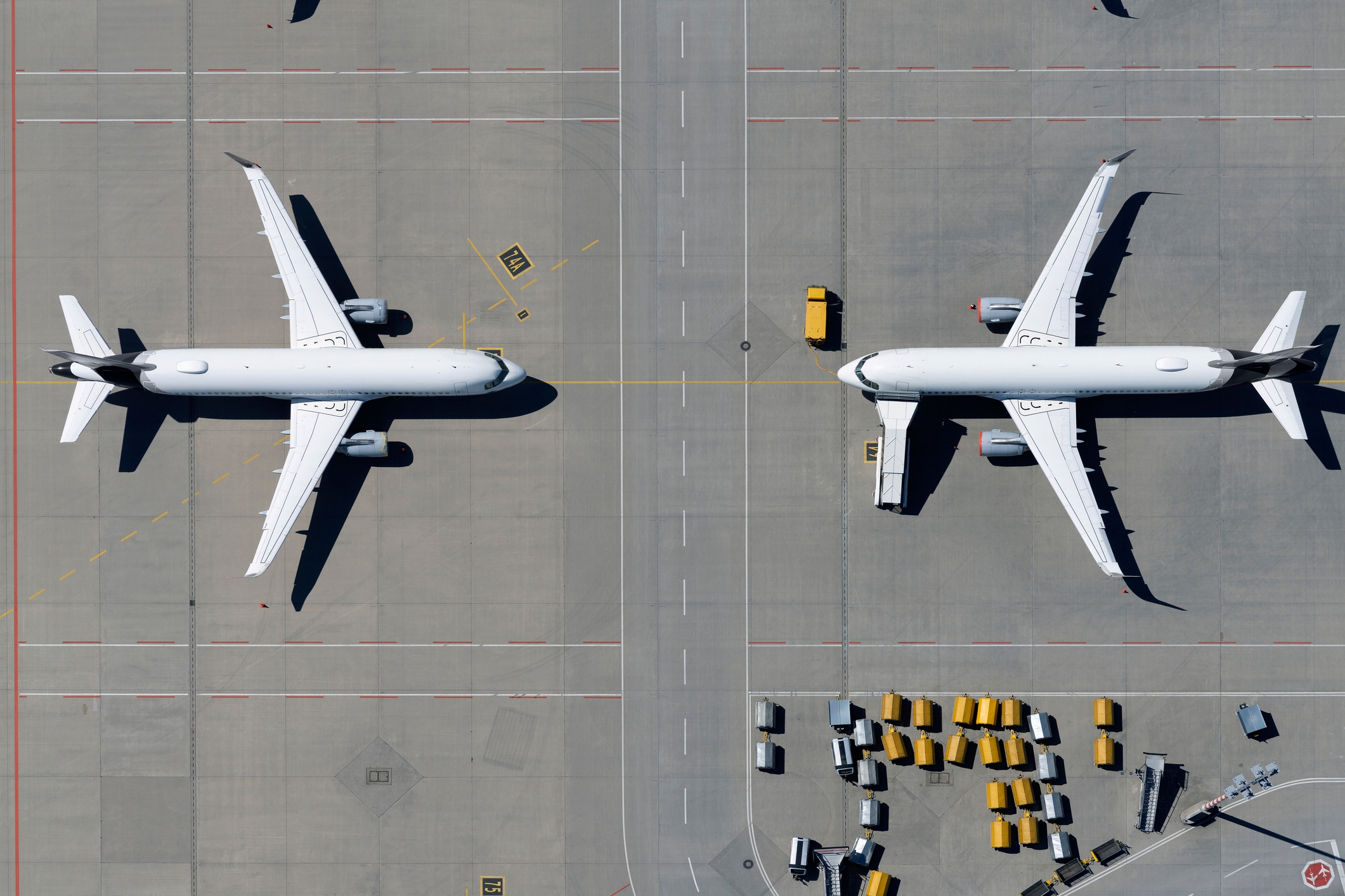 Two commercialized  airplanes parked connected  an airdrome  tarmac, viewed from above, with tiny  work  vehicles nearby