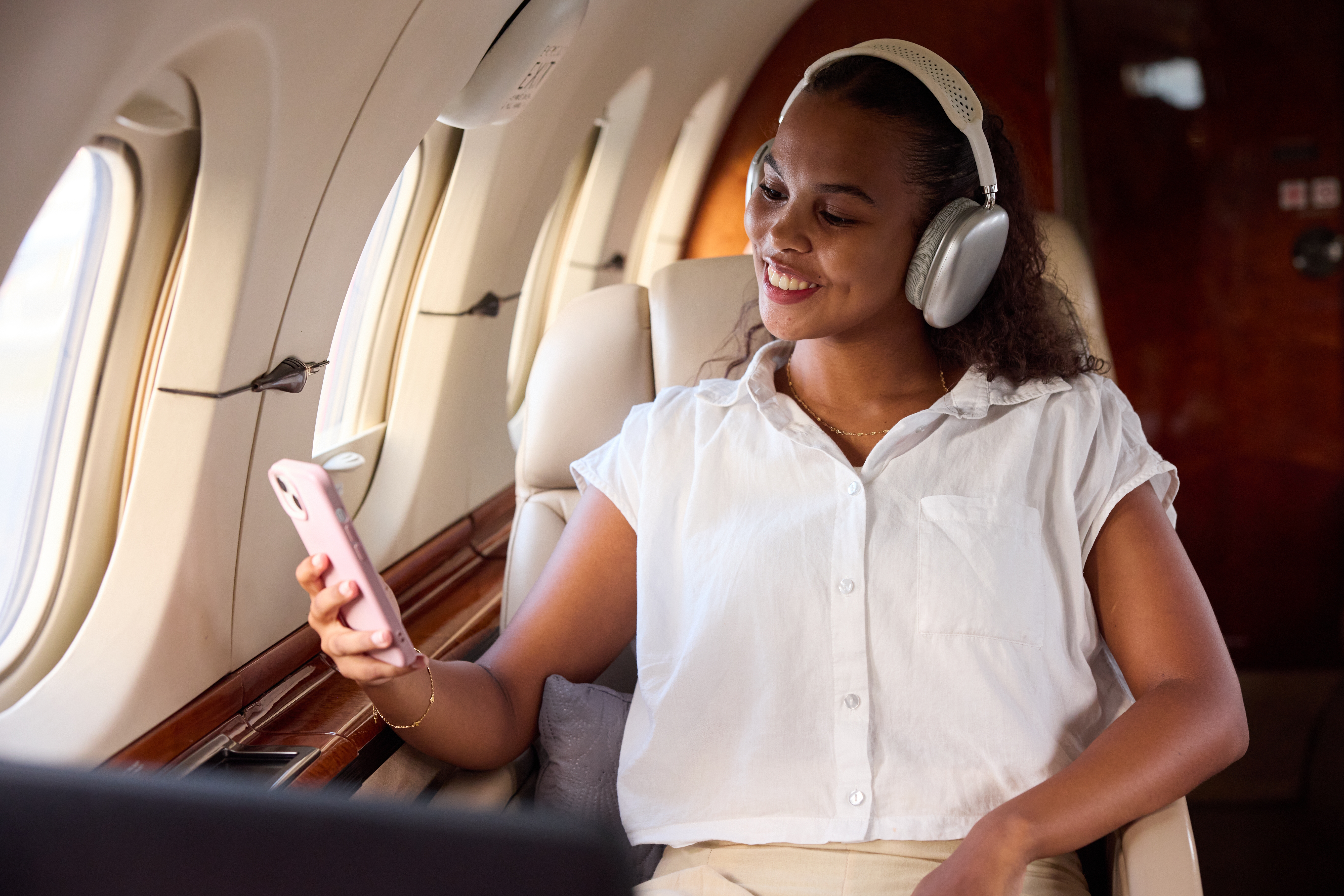 Person successful  a backstage  pitchy  smiling, wearing headphones and a casual shirt, looking astatine  a smartphone