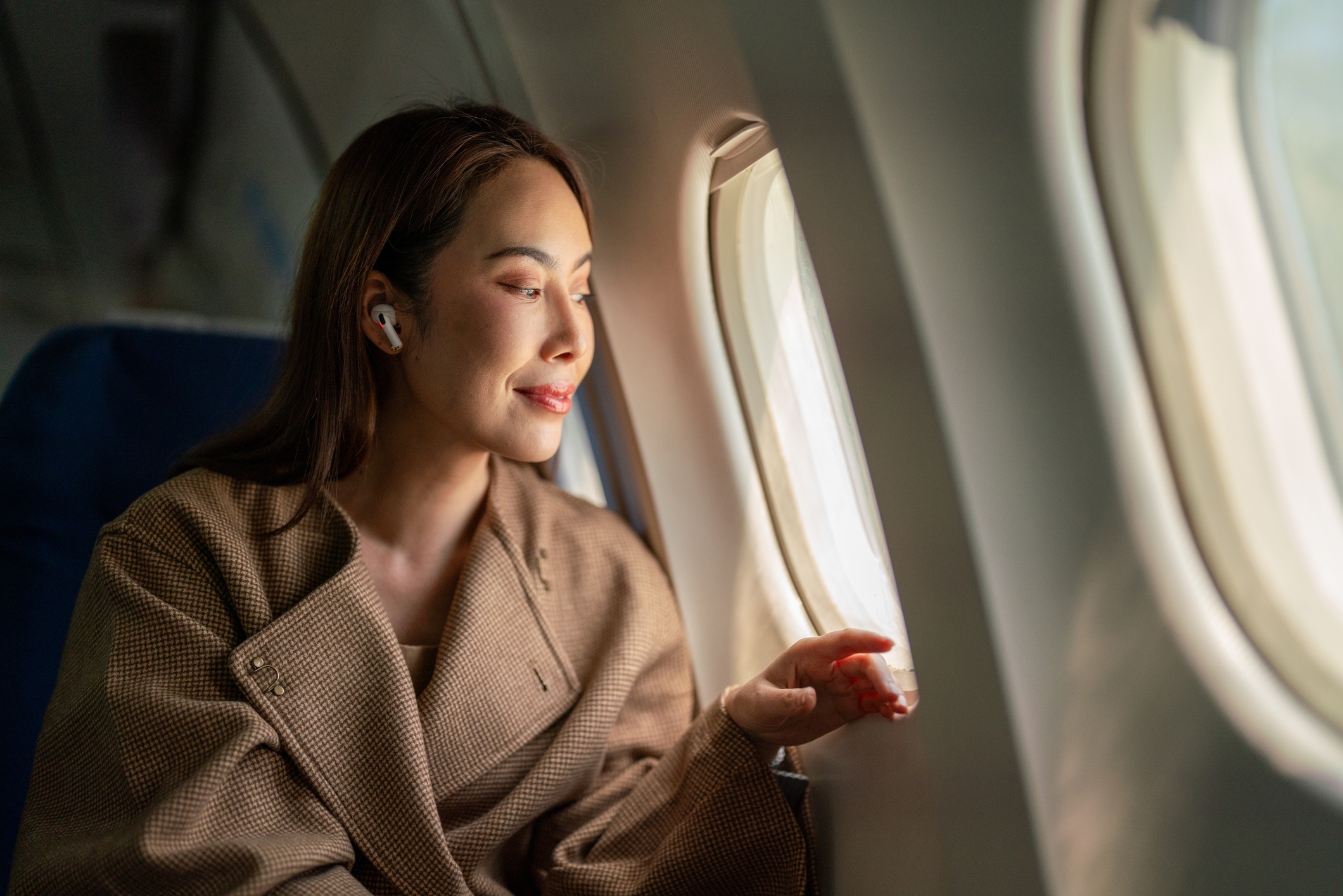 Person sitting connected  an airplane, looking retired  the model   with a thoughtful expression, wearing earbuds and a warm, textured coat