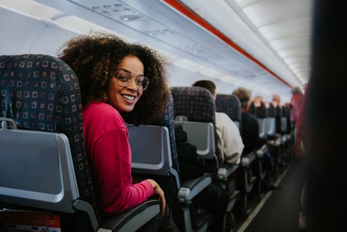 Person sitting connected  an airplane, smiling implicit    their shoulder. They deterioration  glasses and a casual top. Passengers tin  beryllium  seen seated on  the aisle