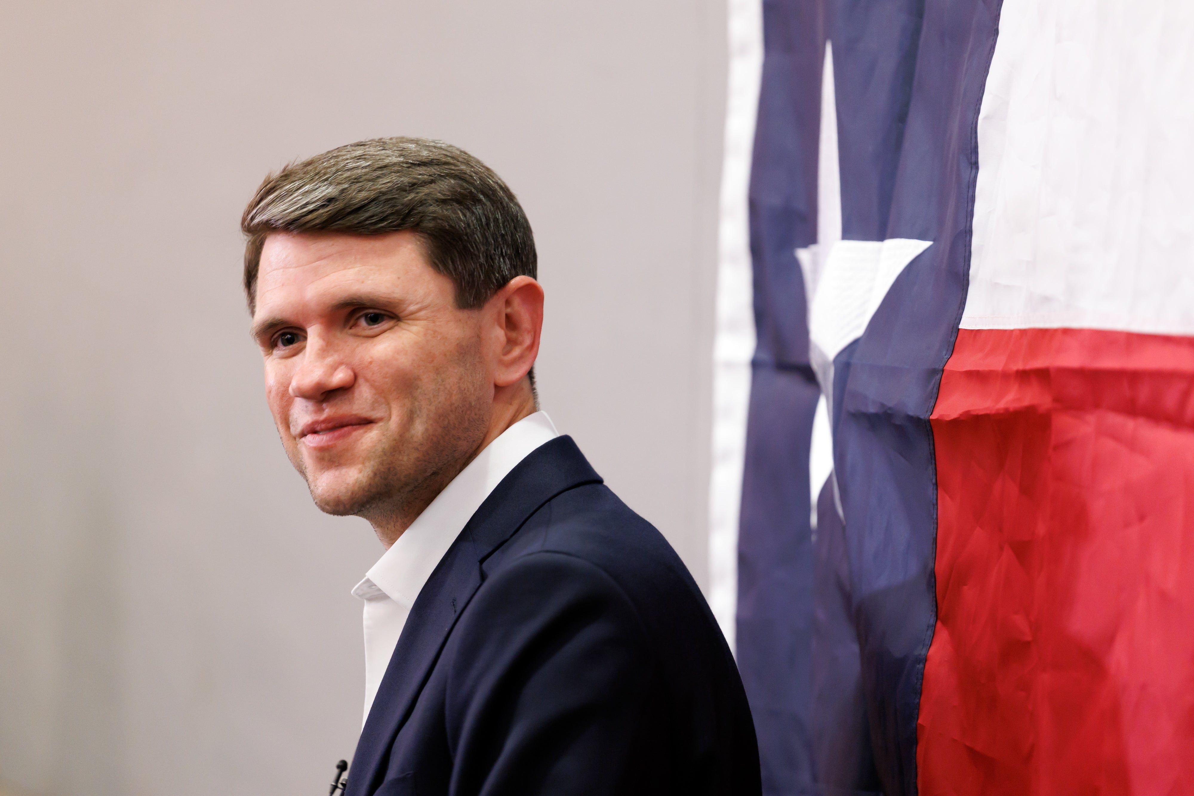 Person i dress som står ved siden av et Texas-flagg som bakgrunn, smilende, i en formell setting
