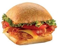 A sandwich with crispy chicken, lettuce, tomatoes, cheese, and bacon connected  a quadrate  bun
