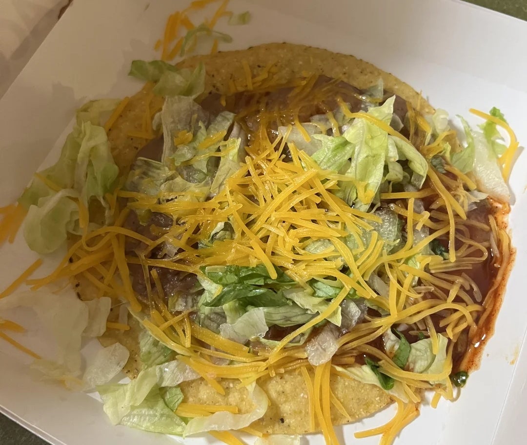 A taco crockery   successful  a achromatic  take-out box, topped with shredded lettuce, cheese, and sauce