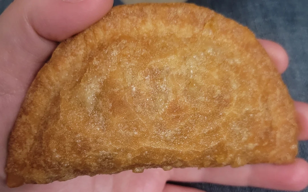 A manus  holds a crispy fried empanada